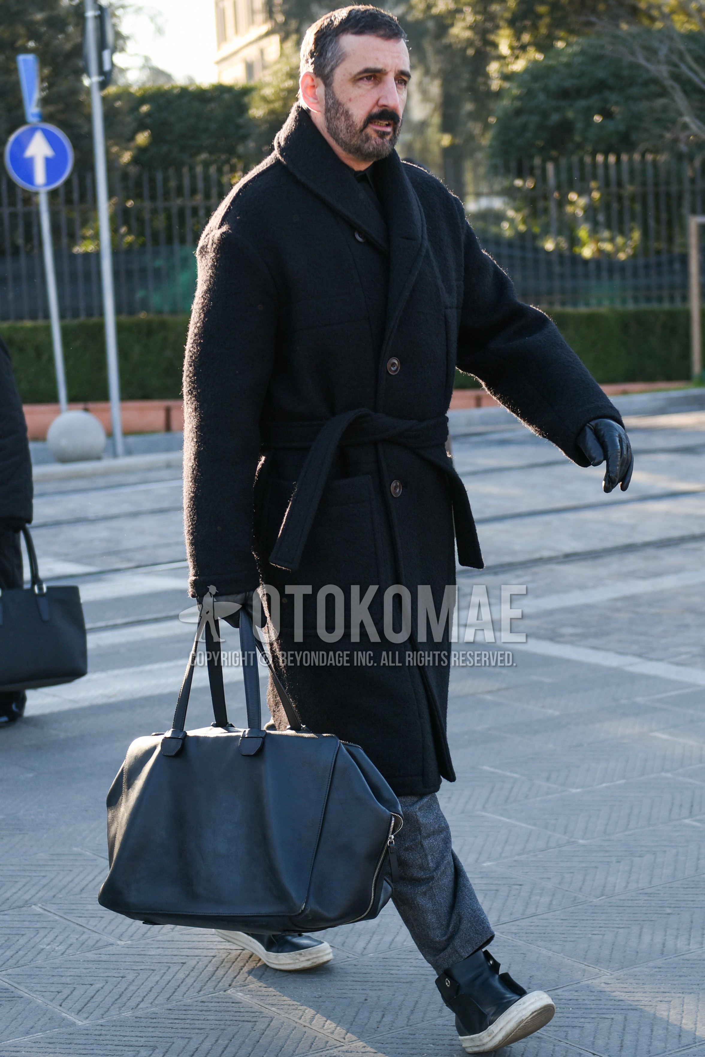 Men's autumn winter outfit with black plain belted coat, gray plain slacks, black high-cut sneakers, dark gray plain briefcase/handbag.