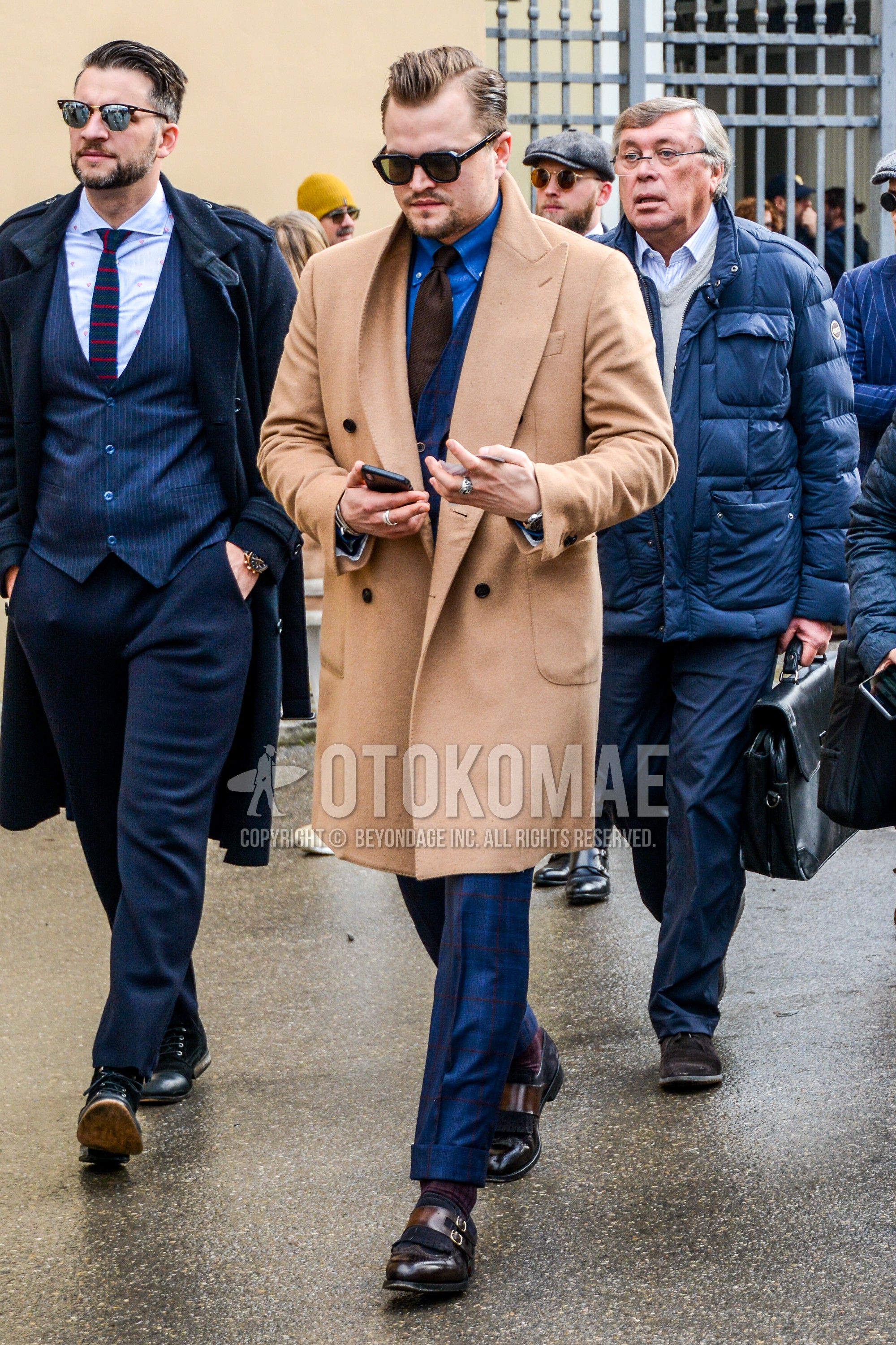 Men's autumn winter outfit with plain sunglasses, beige plain chester coat, blue plain shirt, brown monk shoes leather shoes, navy check three-piece suit, brown plain necktie.