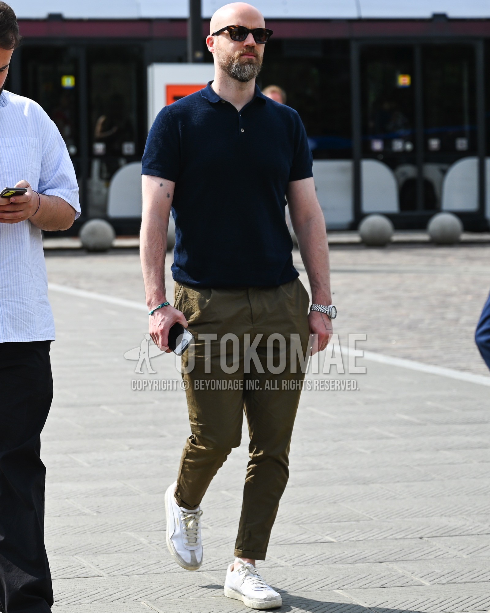 Men's spring summer outfit with black plain sunglasses, navy plain polo shirt, olive green plain chinos, white low-cut sneakers.
