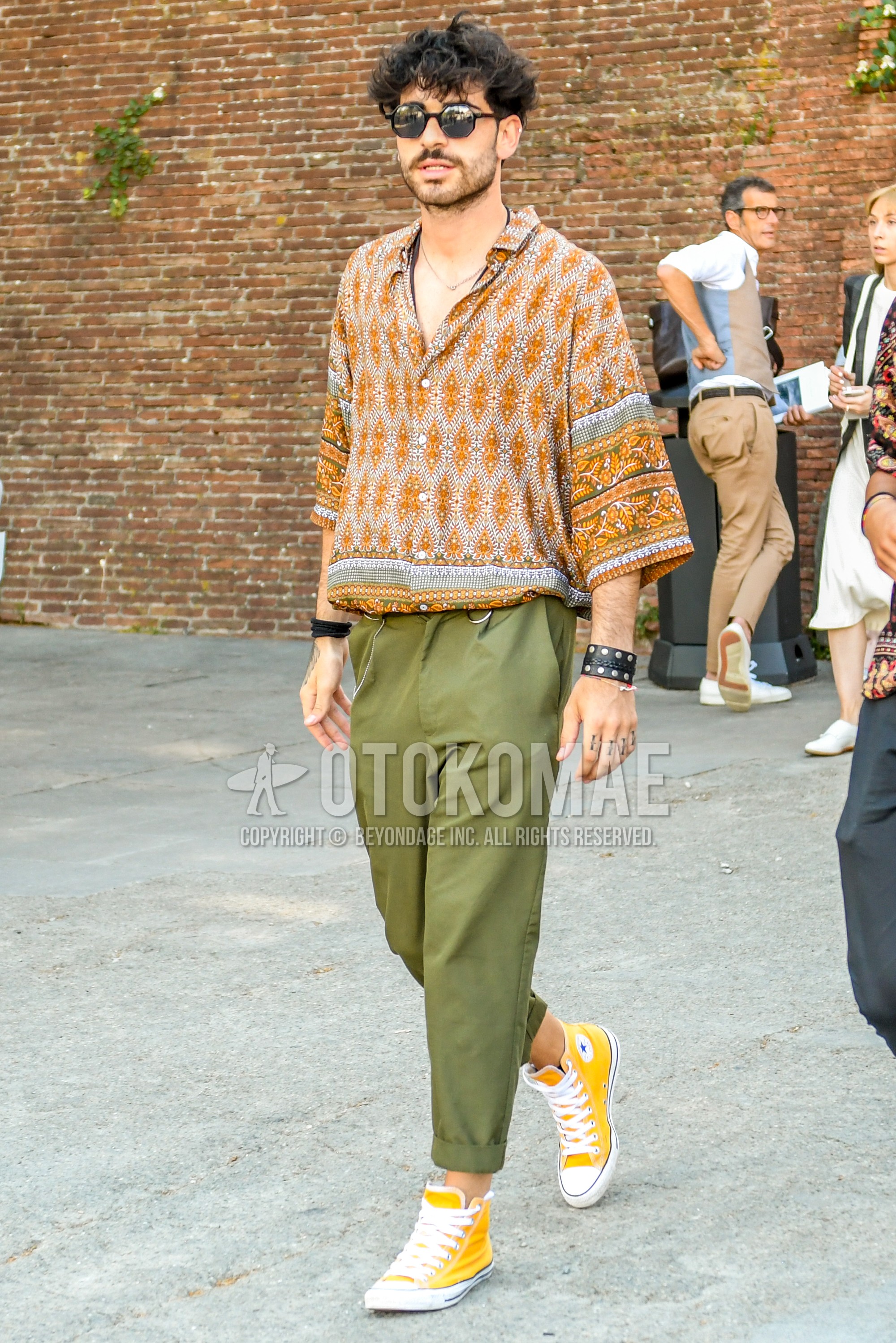 Men's spring summer outfit with plain sunglasses, orange tops/innerwear shirt, olive green plain chinos, yellow high-cut sneakers.