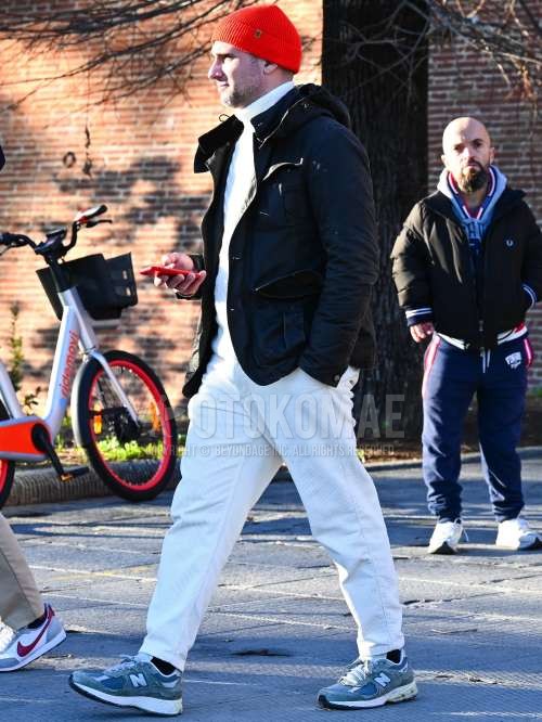 オレンジ無地のニットキャップ、黒無地のフーデッドコート、黒無地のミリタリージャケット(MA-1、M-65以外)、白無地のタートルネックニット、白無地の冬パンツ(コーデュロイ,ベロア)、黒無地のソックス、ニューバランスのグレーローカットのスニーカーを合わせた秋冬のメンズコーデ・着こなし。