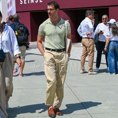 ブラウンべっ甲のサングラス、ニットのグリーン無地のポロシャツ、黒無地のレザーベルト、ベージュ無地のスラックス、ベージュ無地のチノパン、ブラウンローファーの革靴、白バッグのトートバッグを合わせた夏春のメンズコーデ・着こなし。