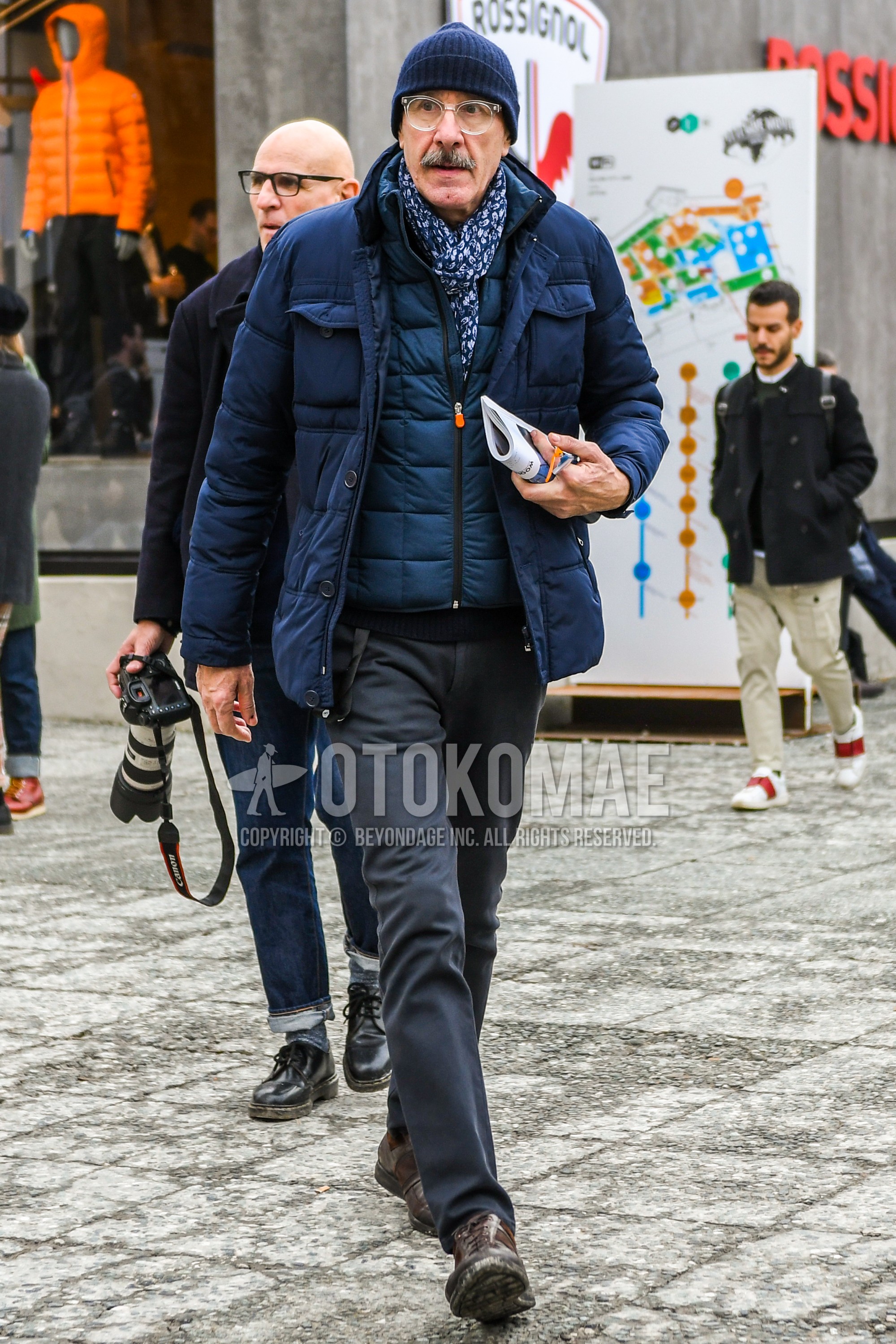 Men's winter outfit with navy plain knit cap, clear plain glasses, blue scarf scarf, navy plain down jacket, navy plain inner down, dark gray plain slacks, brown leather shoes.