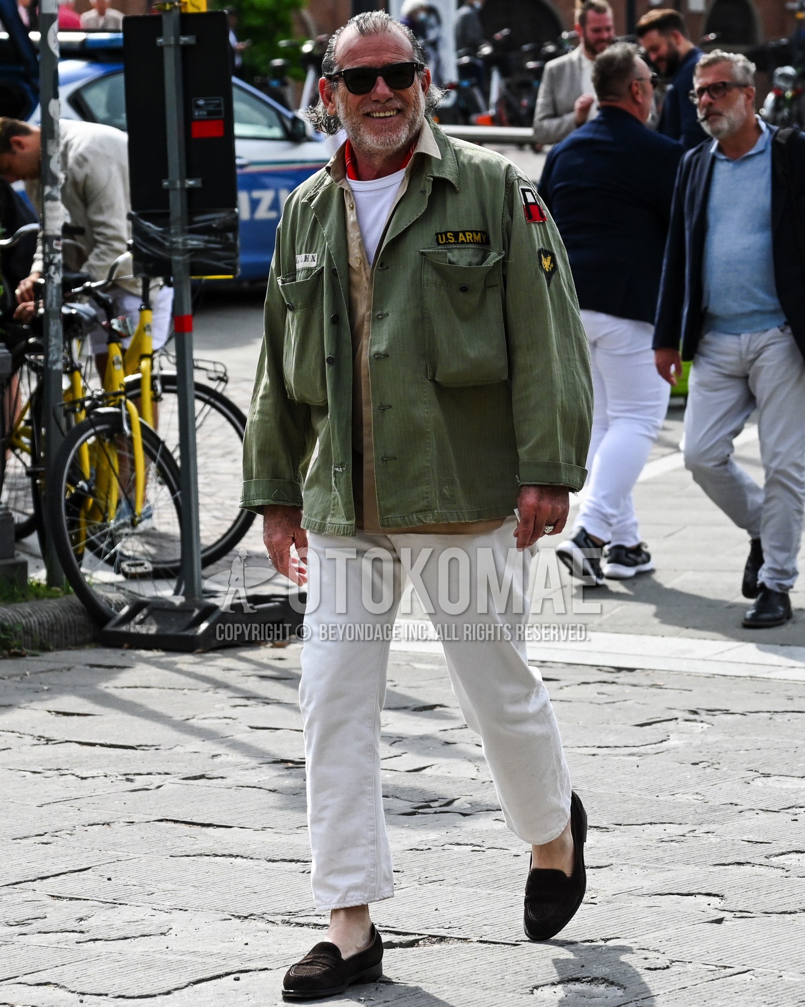 Men's spring summer autumn outfit with black plain sunglasses, olive green one point military jacket, beige plain shirt, white plain t-shirt, white plain chinos, brown coin loafers leather shoes.
