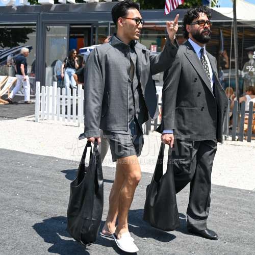 ブラウン無地のサングラス、スタンドカラーのグレー無地のシャツジャケット、グレー無地のシャツ、グレー無地のショートパンツ、白サンダル、レザーの黒無地のトートバッグを合わせた夏春のメンズコーデ・着こなし。