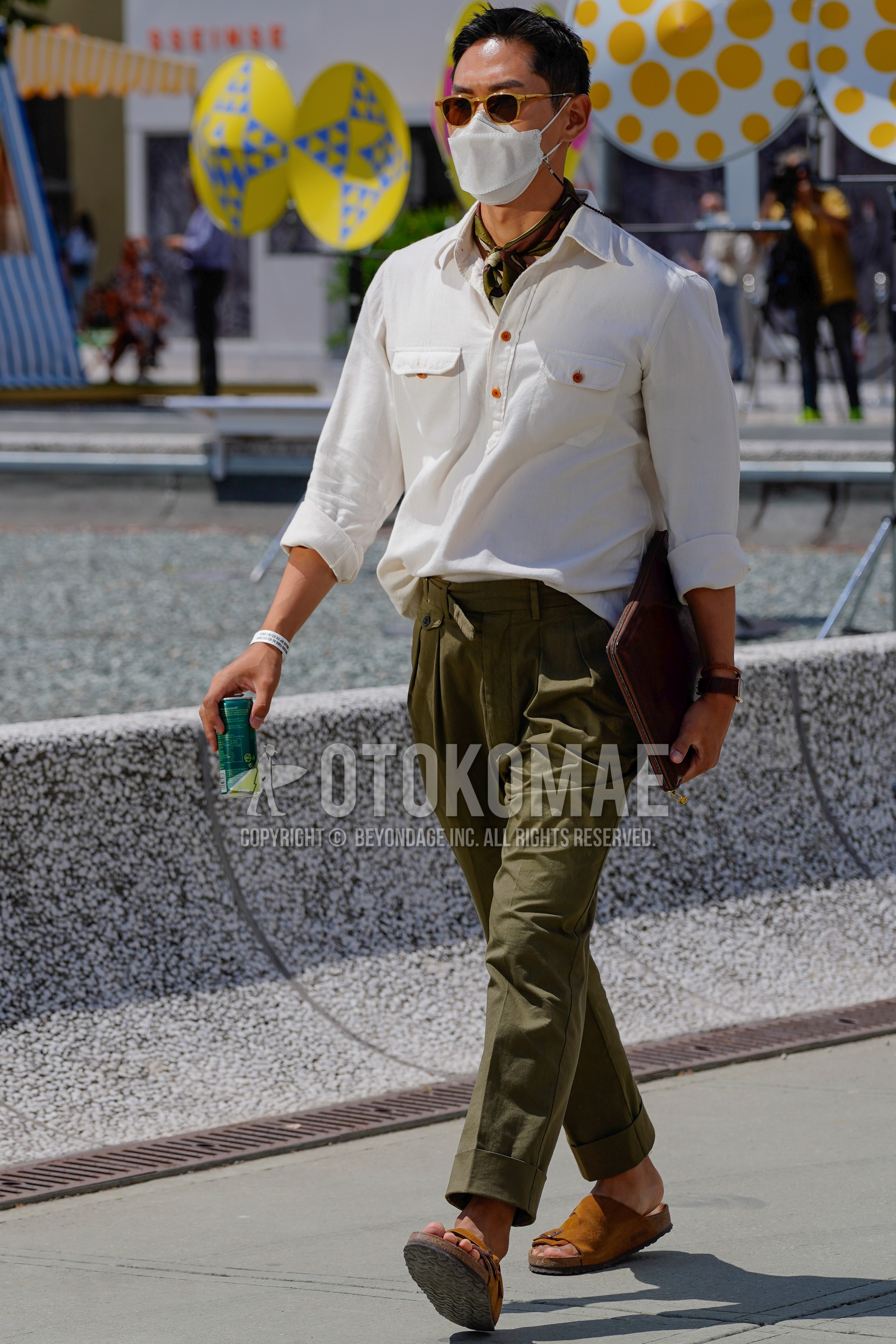 Men's spring summer outfit with brown tortoiseshell sunglasses, olive green plain bandana/neckerchief, white plain shirt, olive green plain slacks, brown leather sandals, brown plain clutch bag/second bag/drawstring bag.