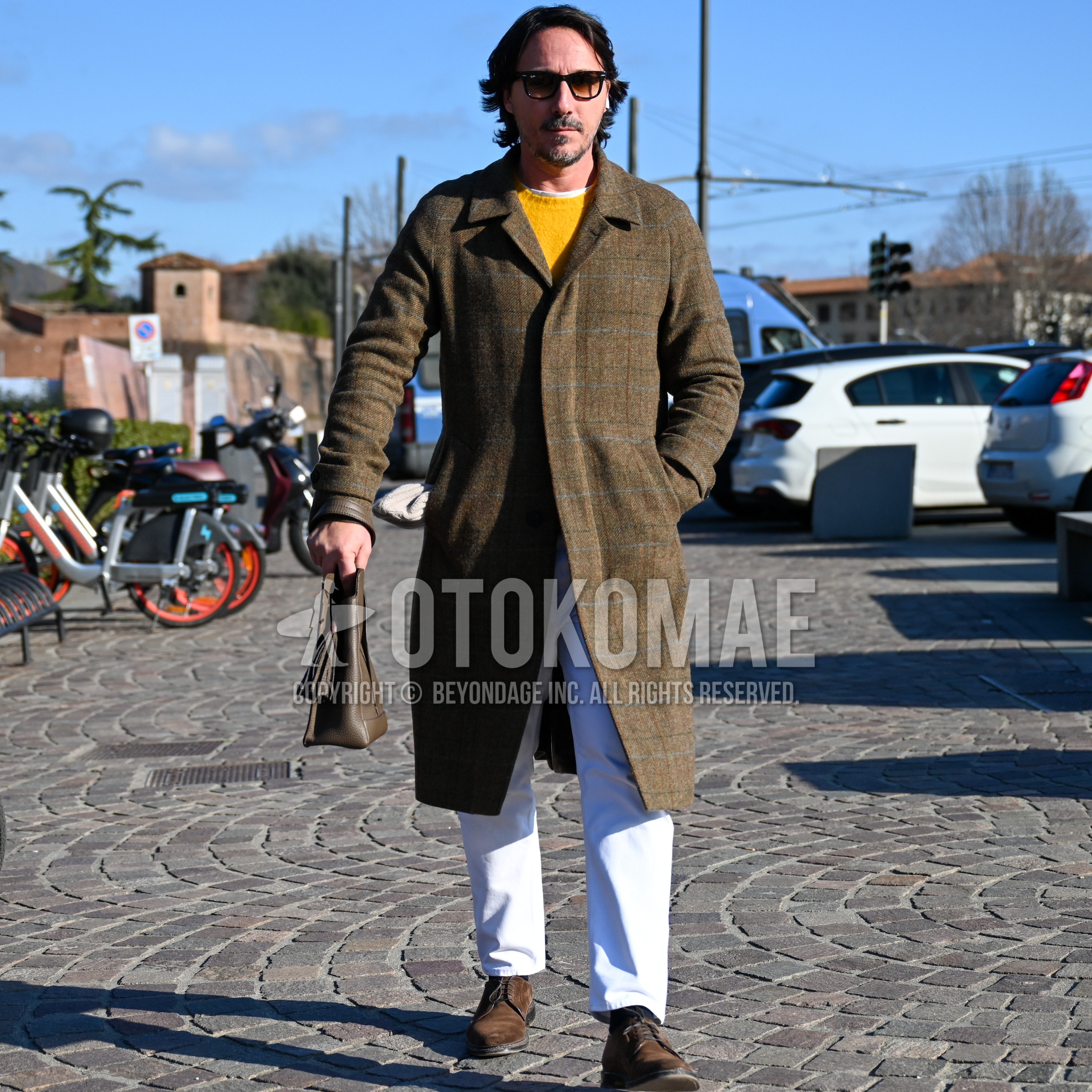 Men's autumn winter outfit with black plain sunglasses, olive green check chester coat, white plain long sleeve t-shirt, yellow plain sweater, white plain chinos, black plain socks, brown suede shoes leather shoes, olive green plain briefcase/handbag.