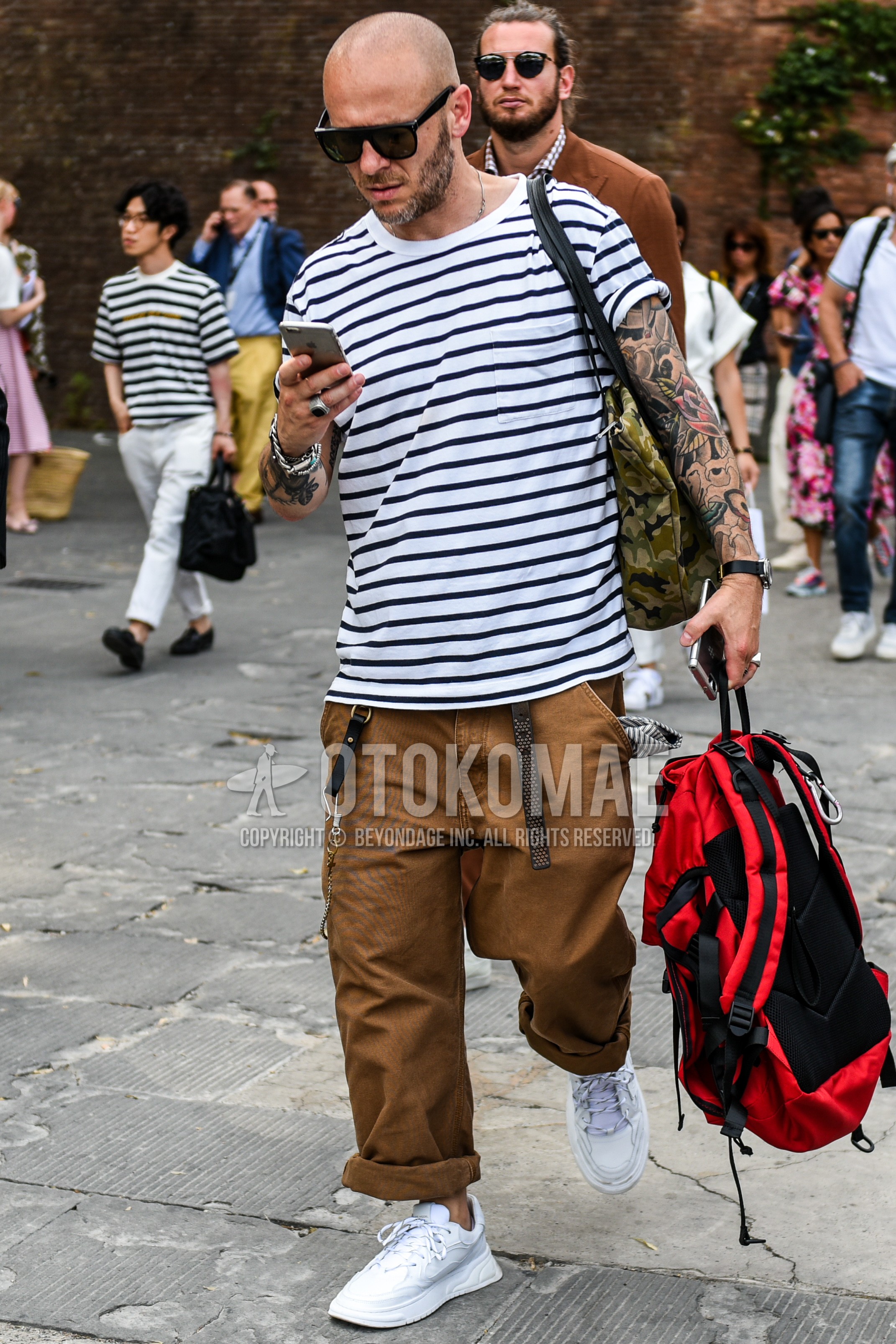 Men's summer outfit with plain sunglasses, white horizontal stripes t-shirt, brown plain cotton pants, white low-cut sneakers.