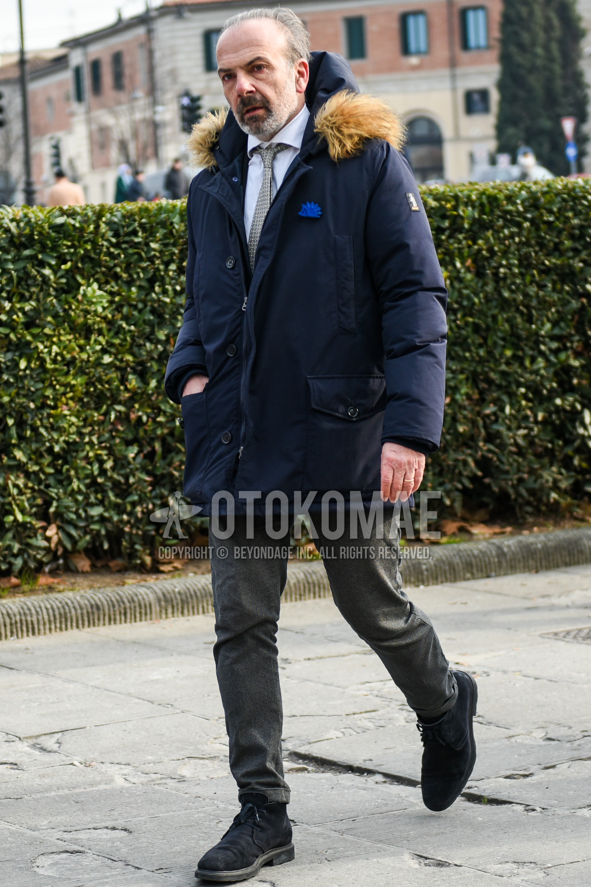 Men's winter outfit with navy plain down jacket, white plain shirt, gray plain slacks, black chukka boots, gray necktie necktie.