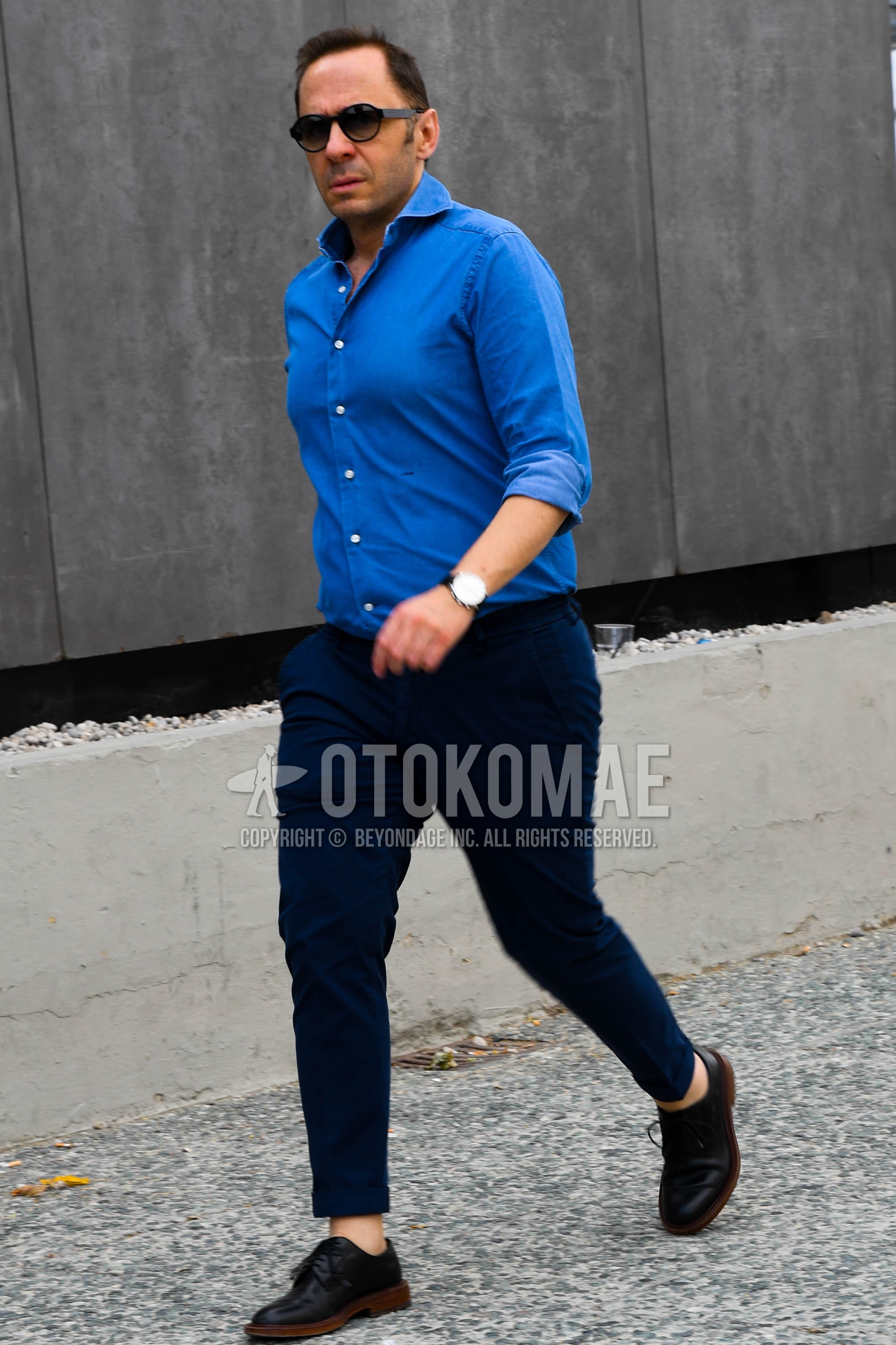 Men's spring summer outfit with plain sunglasses, blue plain shirt, navy plain chinos, black plain toe leather shoes.