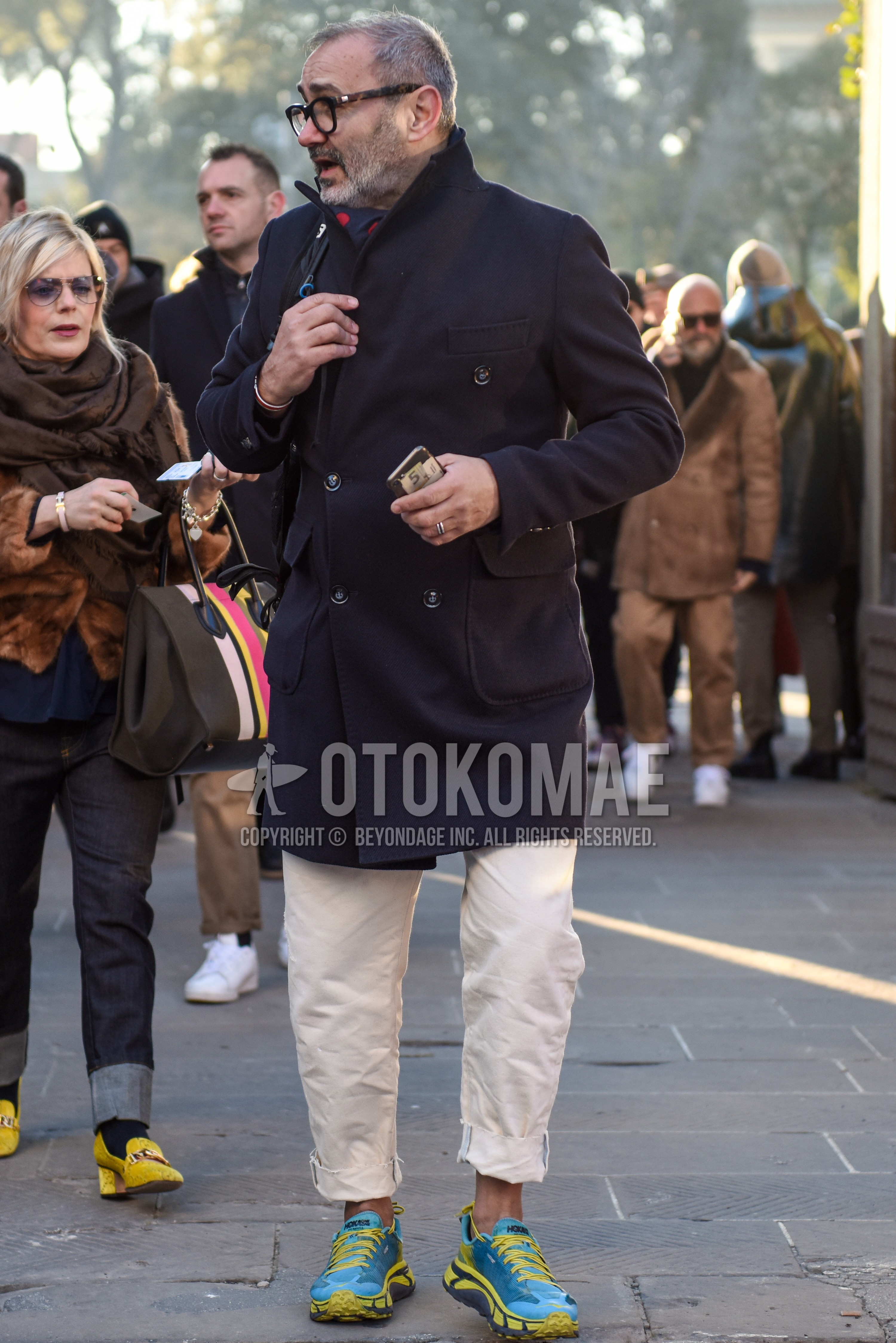 Men's autumn winter outfit with brown tortoiseshell glasses, gray scarf scarf, dark gray plain chester coat, white plain cotton pants, light blue yellow low-cut sneakers.