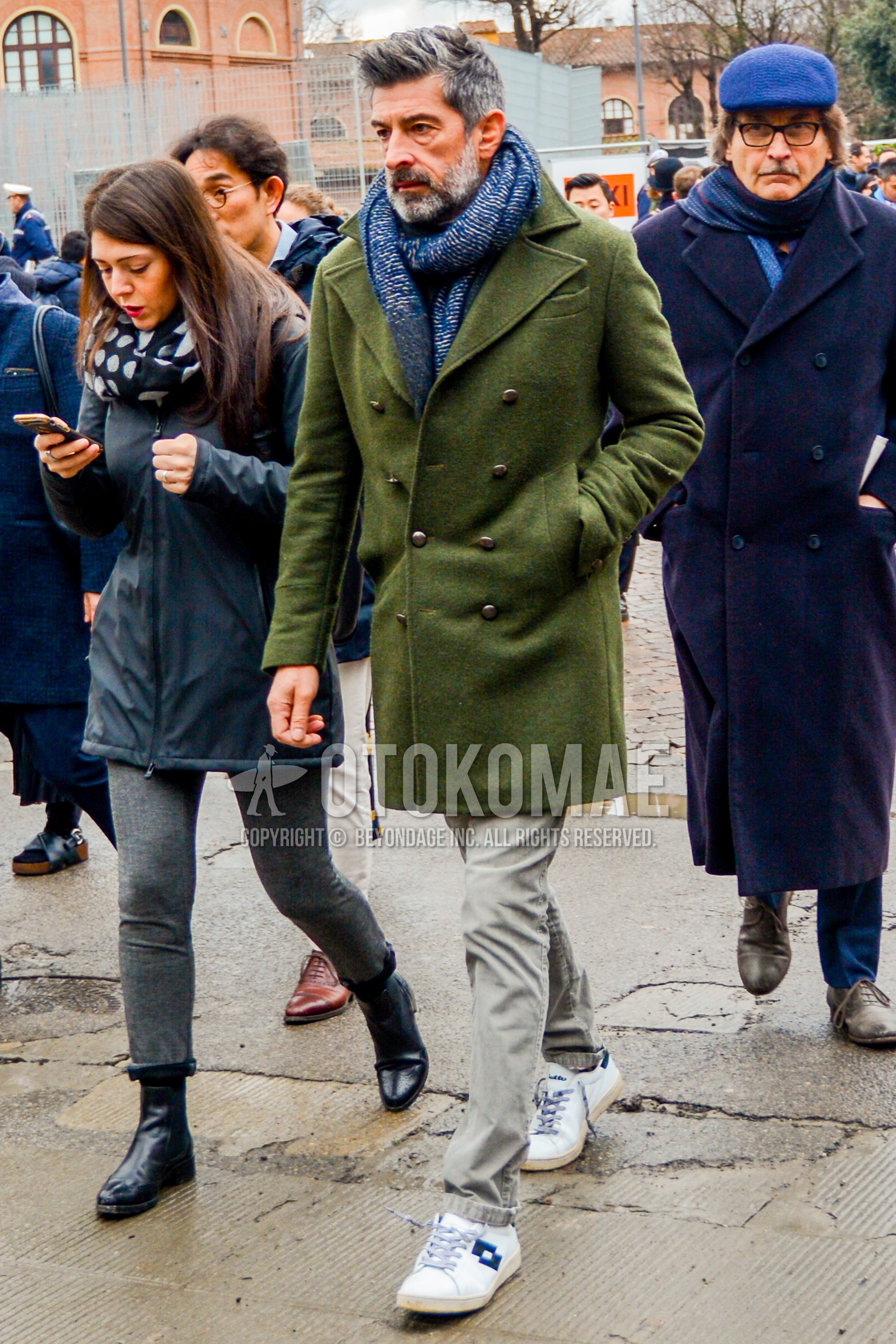Men's winter outfit with blue plain scarf, olive green plain p coat, gray plain cotton pants, white low-cut sneakers.