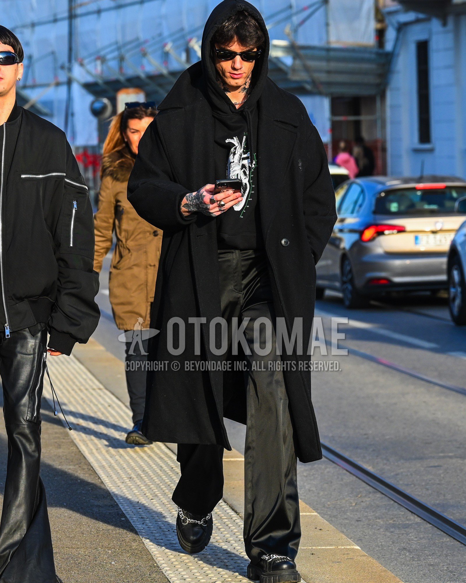 Men's autumn winter outfit with black plain sunglasses, black plain ulster coat, black graphic hoodie, black plain bottoms, black  boots.