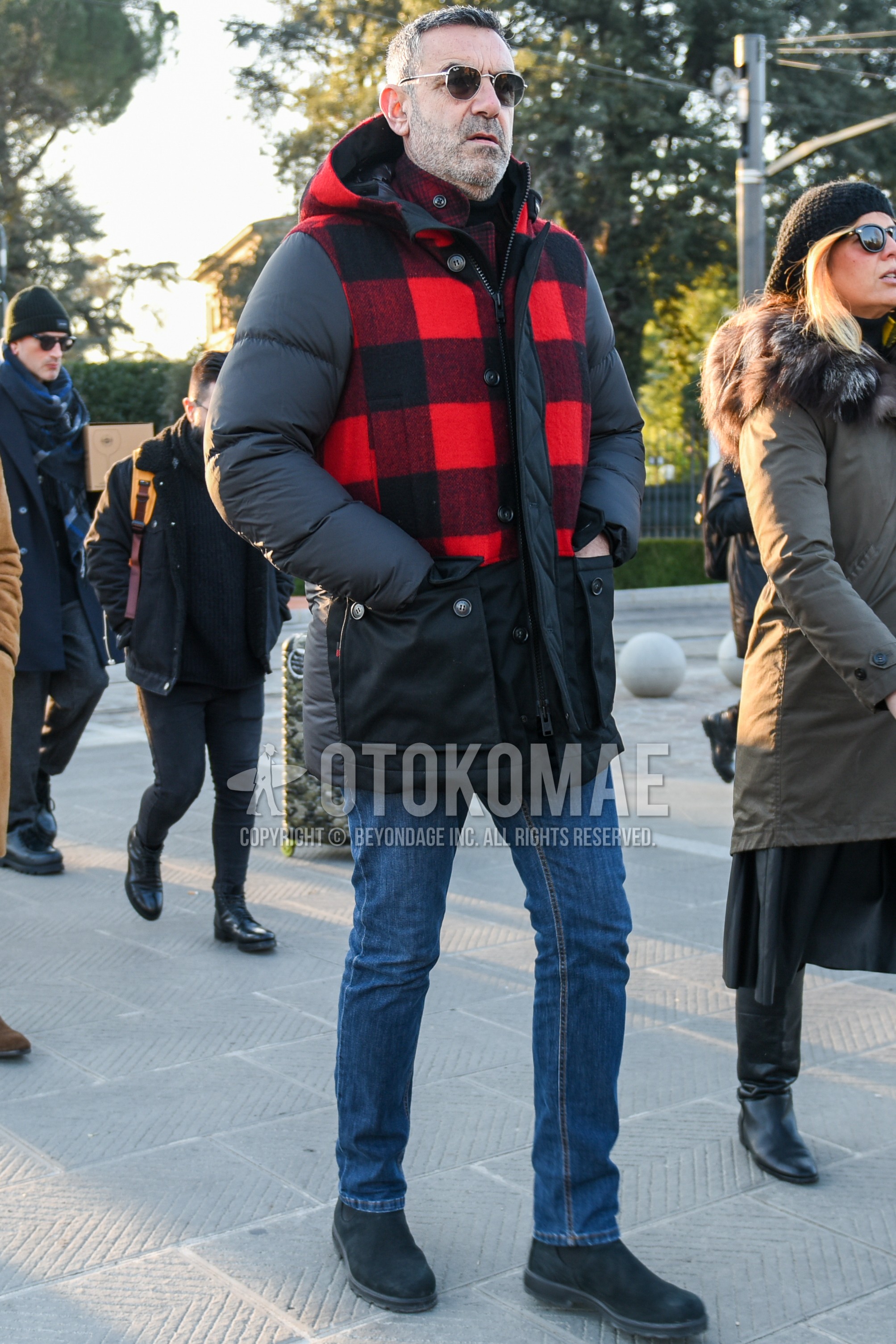 Men's winter outfit with gold plain sunglasses, black red check down jacket, black red check hooded coat, black red check shirt, blue plain denim/jeans, black side-gore boots.