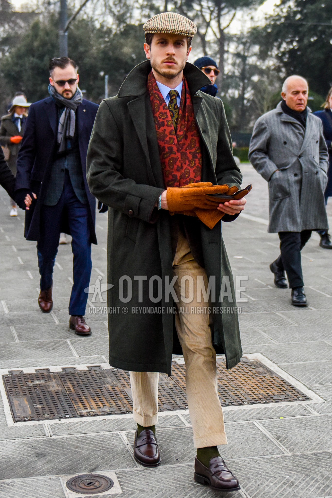 Men's winter outfit with beige check cap, red scarf scarf, olive green plain stenkarrer coat, gray plain tailored jacket, light blue plain shirt, beige plain winter pants (corduroy,velour), olive green plain socks, brown coin loafers leather shoes, olive green paisley knit tie.