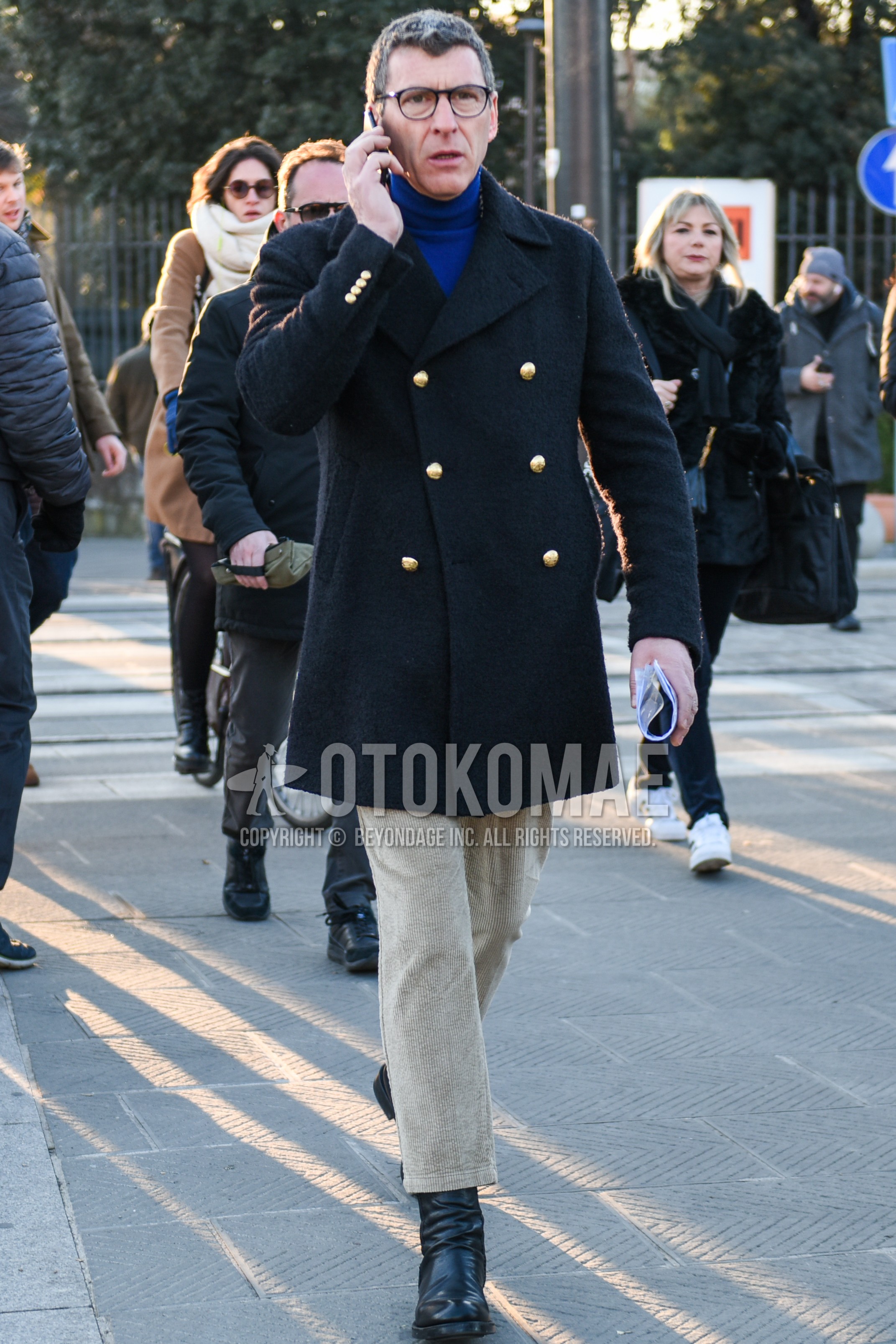 Men's autumn winter outfit with black plain glasses, navy plain p coat, blue plain turtleneck knit, beige plain winter pants (corduroy,velour), beige plain cropped pants, black side-gore boots.