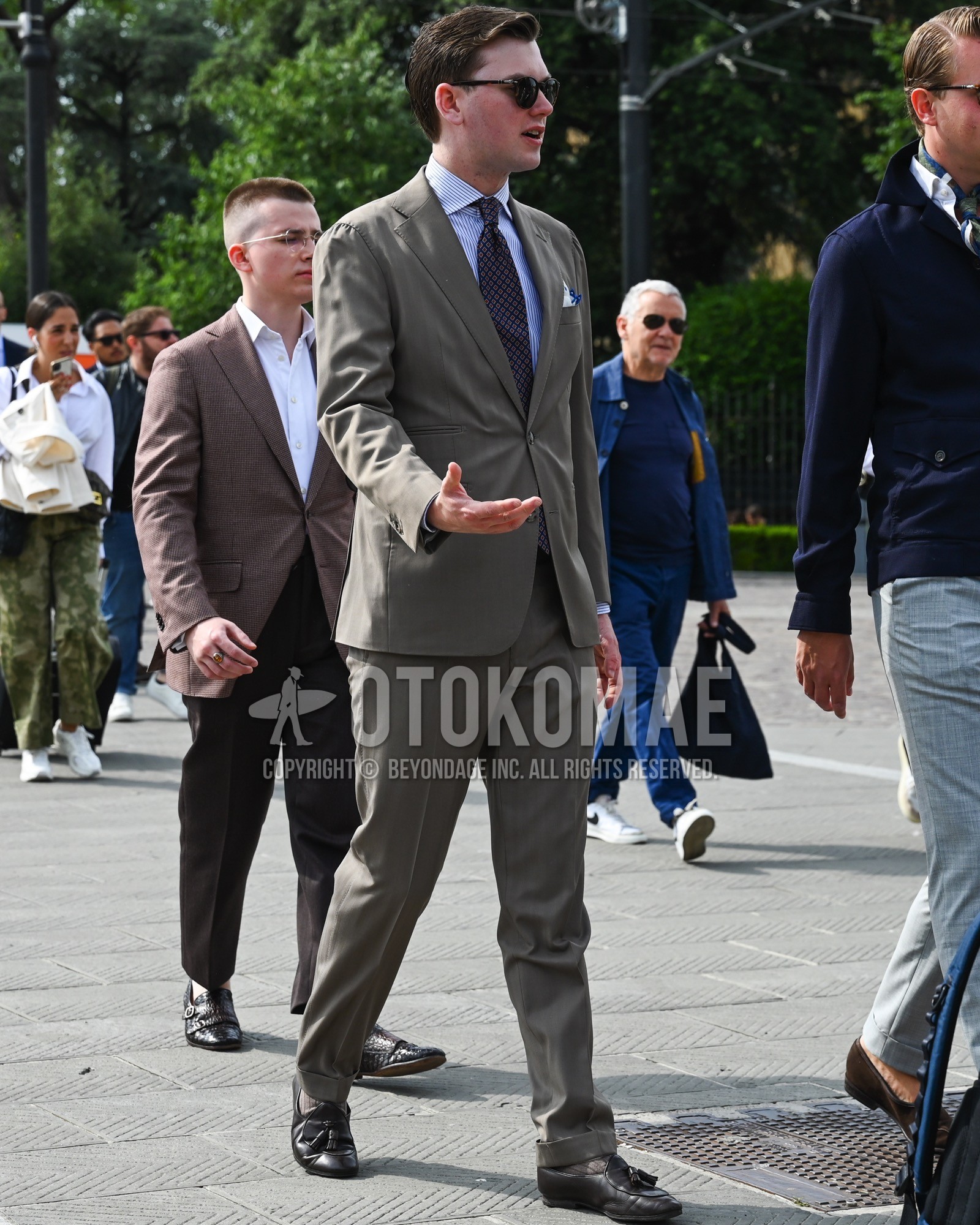 Men's spring summer autumn outfit with black plain sunglasses, light blue plain shirt, brown plain socks, dark gray plain suit, navy small crest necktie.