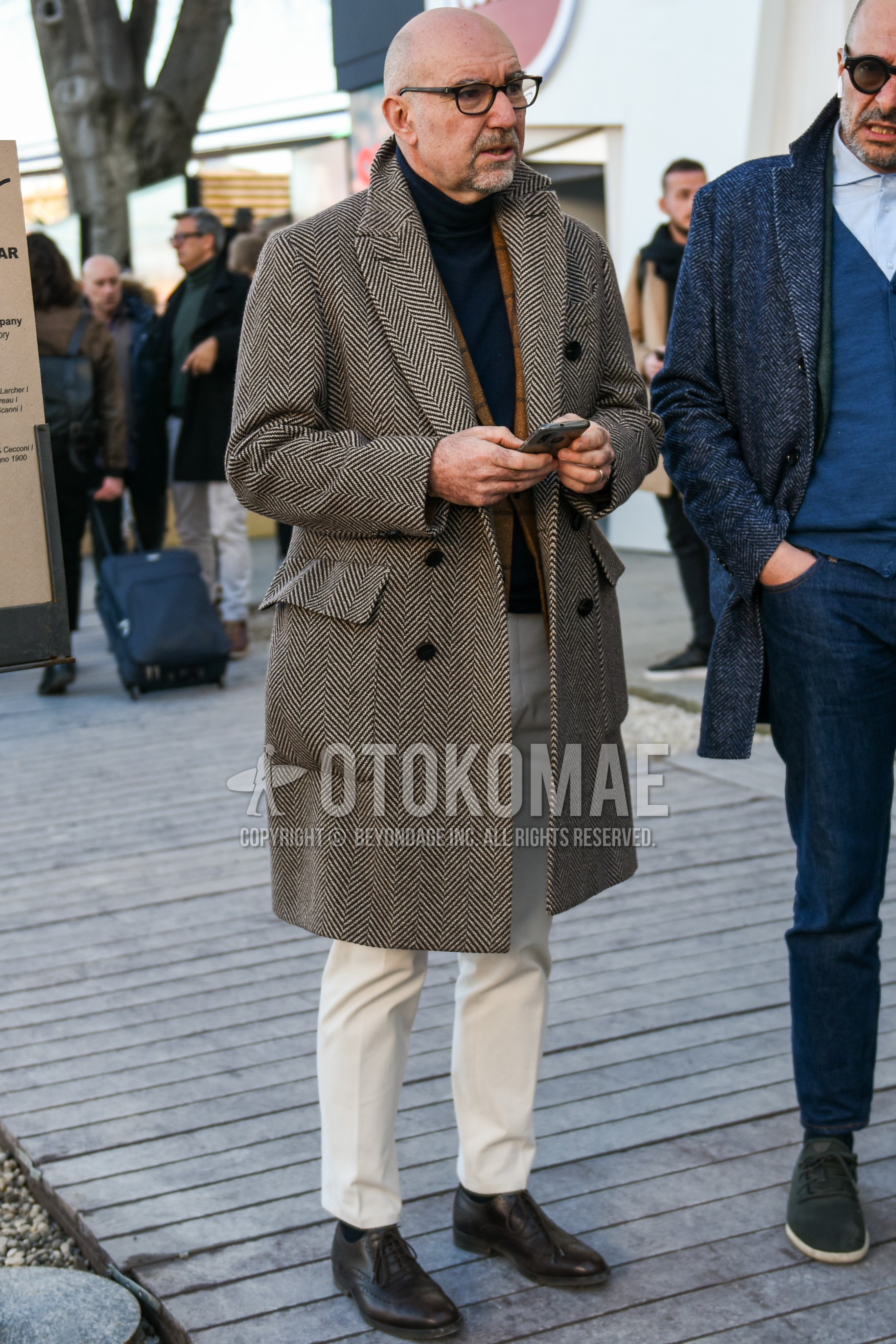 Men's autumn winter outfit with black plain glasses, gray herringbone chester coat, beige check tailored jacket, navy plain turtleneck knit, white plain cotton pants, white plain ankle pants, navy plain socks, brown brogue shoes leather shoes.