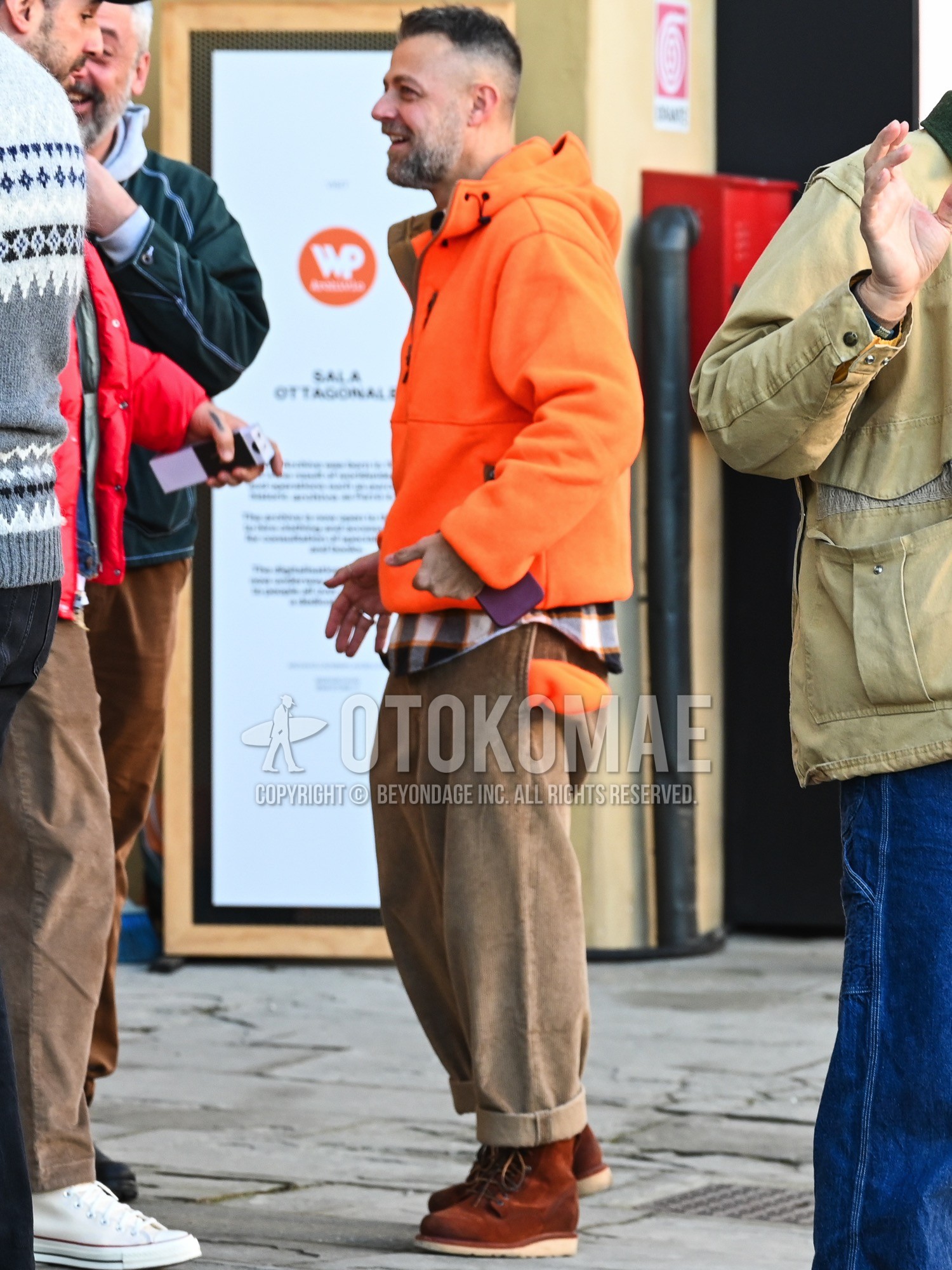 Men's autumn winter outfit with orange plain mountain parka, black white orange check shirt, brown plain winter pants (corduroy,velour), brown work boots.