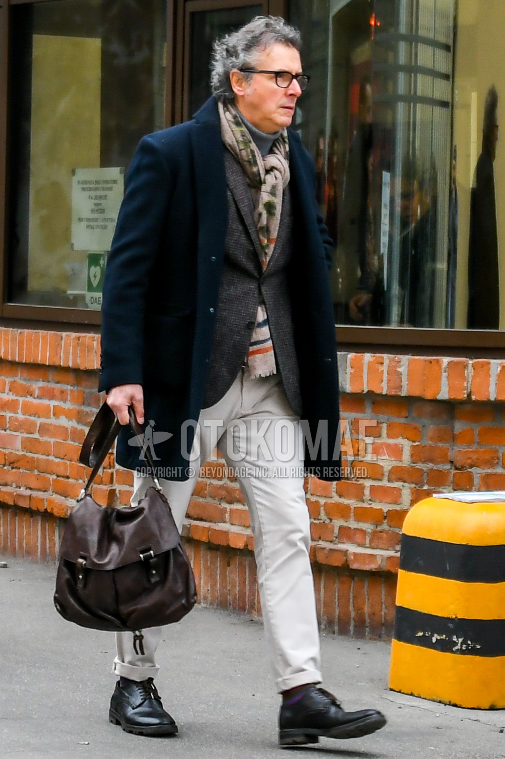 Men's autumn winter outfit with black plain glasses, beige scarf scarf, navy plain chester coat, gray check tailored jacket, gray plain sweater, beige plain chinos, black wing-tip shoes leather shoes, brown plain shoulder bag.