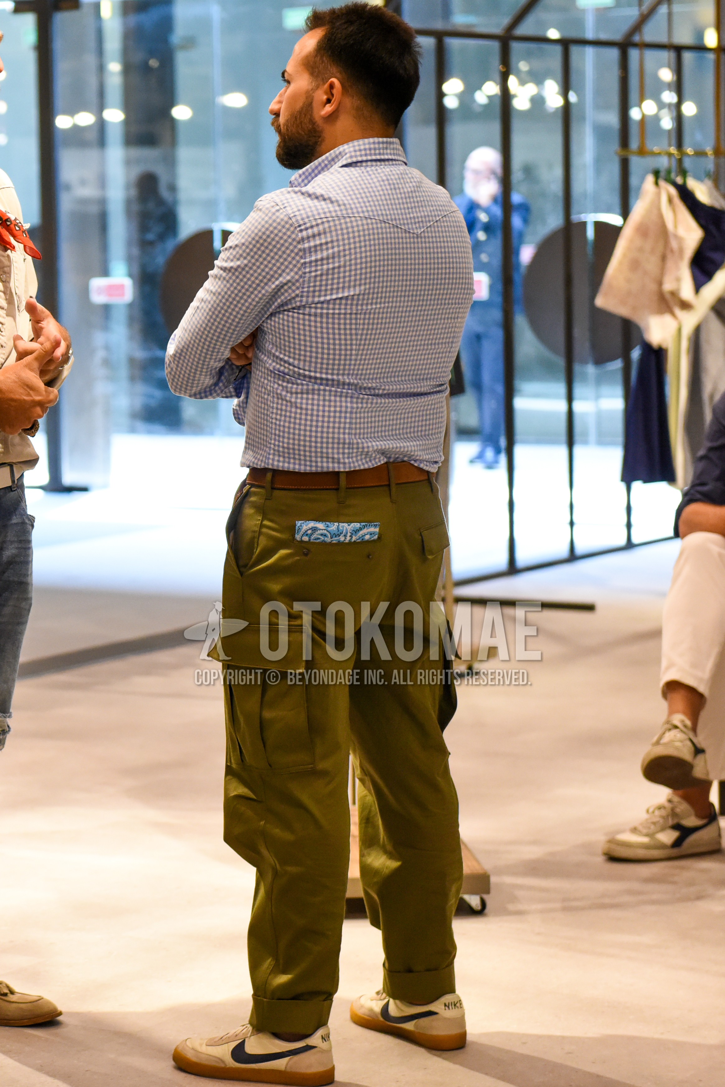 Men's spring summer autumn outfit with white check shirt, brown plain leather belt, olive green plain cargo pants, white low-cut sneakers.
