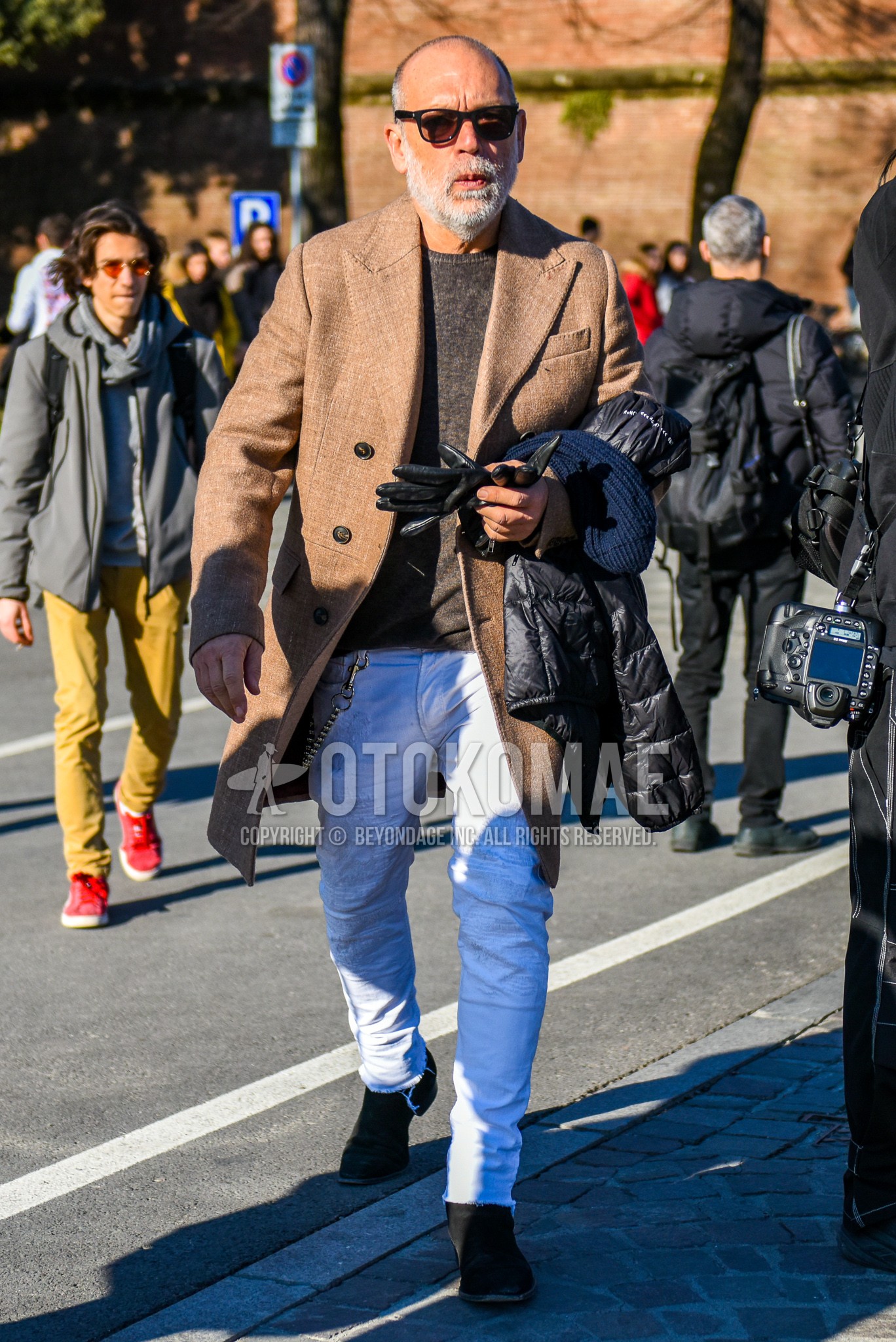 Men's autumn winter outfit with black plain sunglasses, beige plain chester coat, gray plain sweater, white plain damaged jeans, brown side-gore boots.