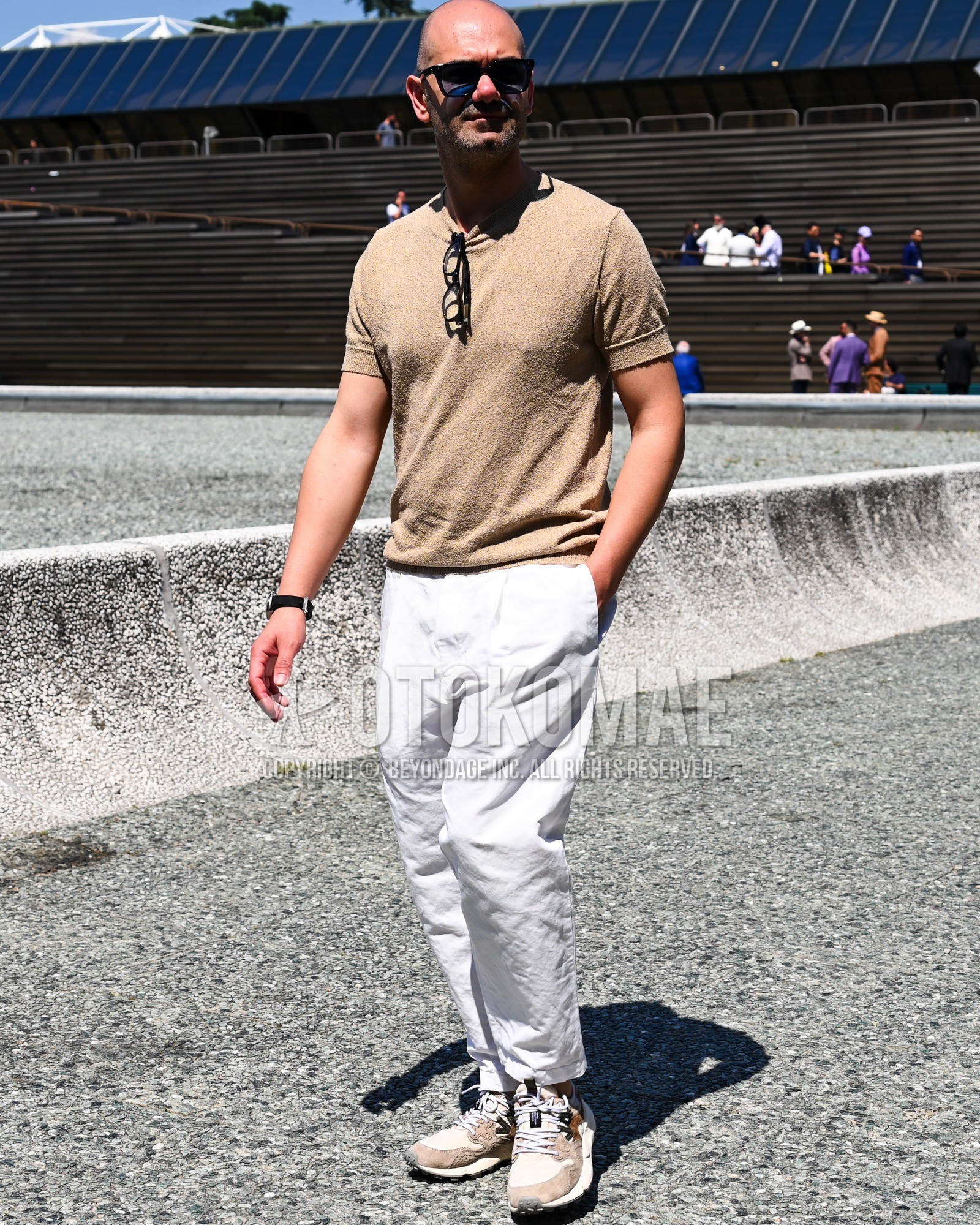Men's spring summer outfit with black plain sunglasses, beige plain polo shirt, white plain chinos, beige low-cut sneakers.