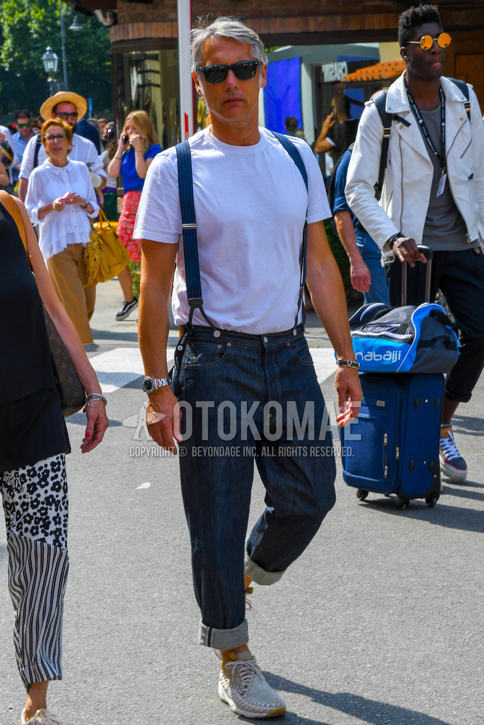 Men's summer outfit with plain sunglasses, white plain t-shirt, navy plain suspenders, navy plain denim/jeans, beige low-cut sneakers.