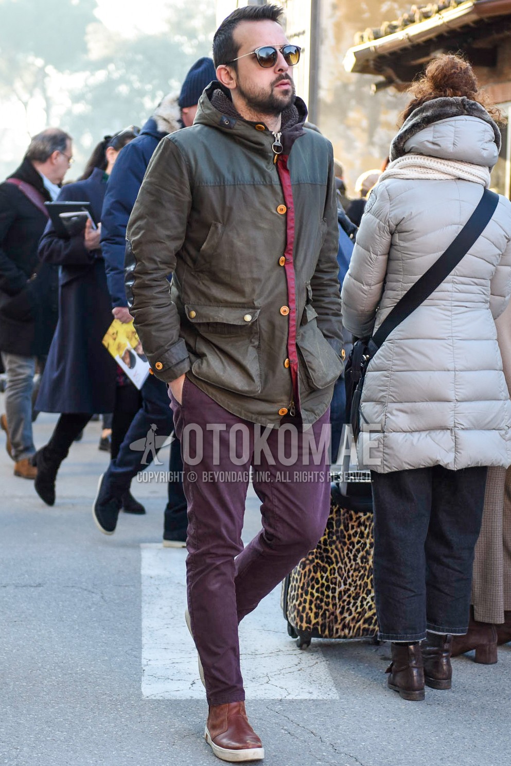 Men's autumn winter outfit with black plain sunglasses, olive green plain hooded coat, purple plain chinos, brown high-cut sneakers.