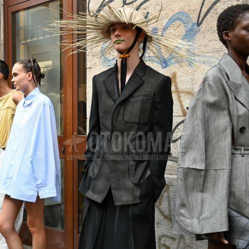 ベージュ無地のキャップ、黒無地のサファリジャケット、黒無地のスラックス、黒無地のプリーツパンツ、黒無地のカジュアルセットアップを合わせた春夏のメンズコーデ・着こなし。