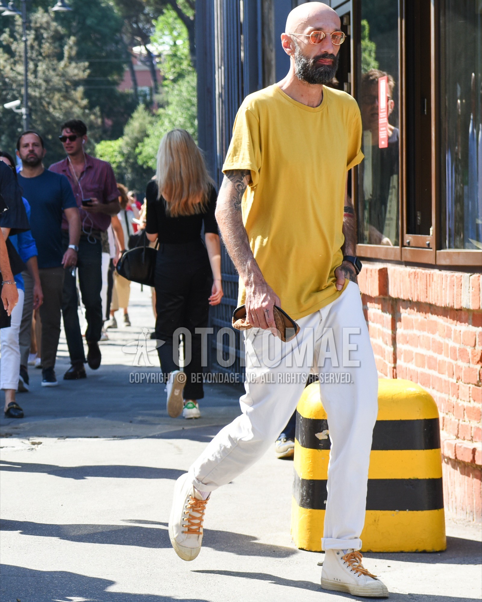 Men's spring summer outfit with gold plain sunglasses, yellow plain t-shirt, white plain cotton pants, white high-cut sneakers.