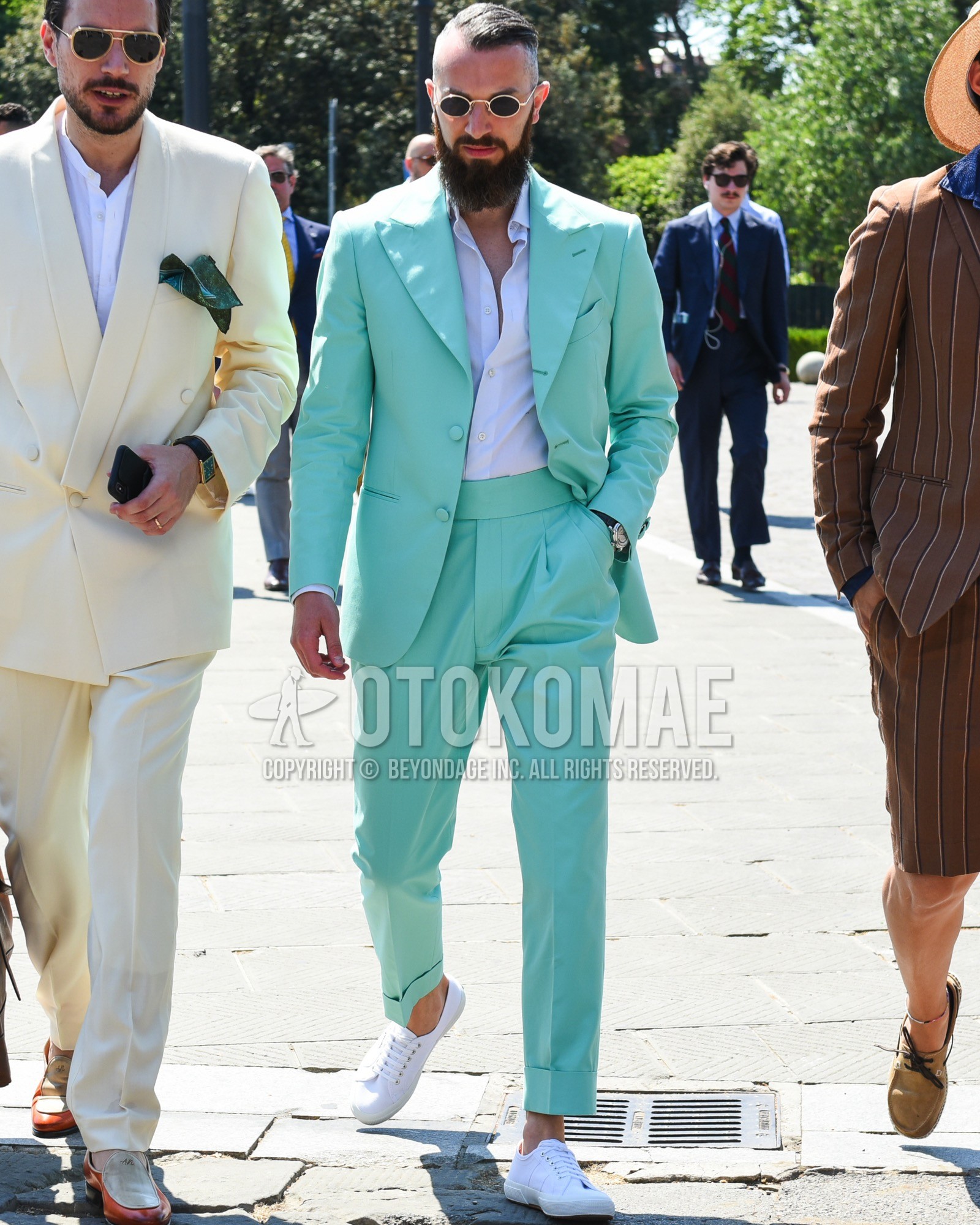 Men's spring summer outfit with gold plain sunglasses, white plain shirt, white low-cut sneakers, green plain three-piece suit.