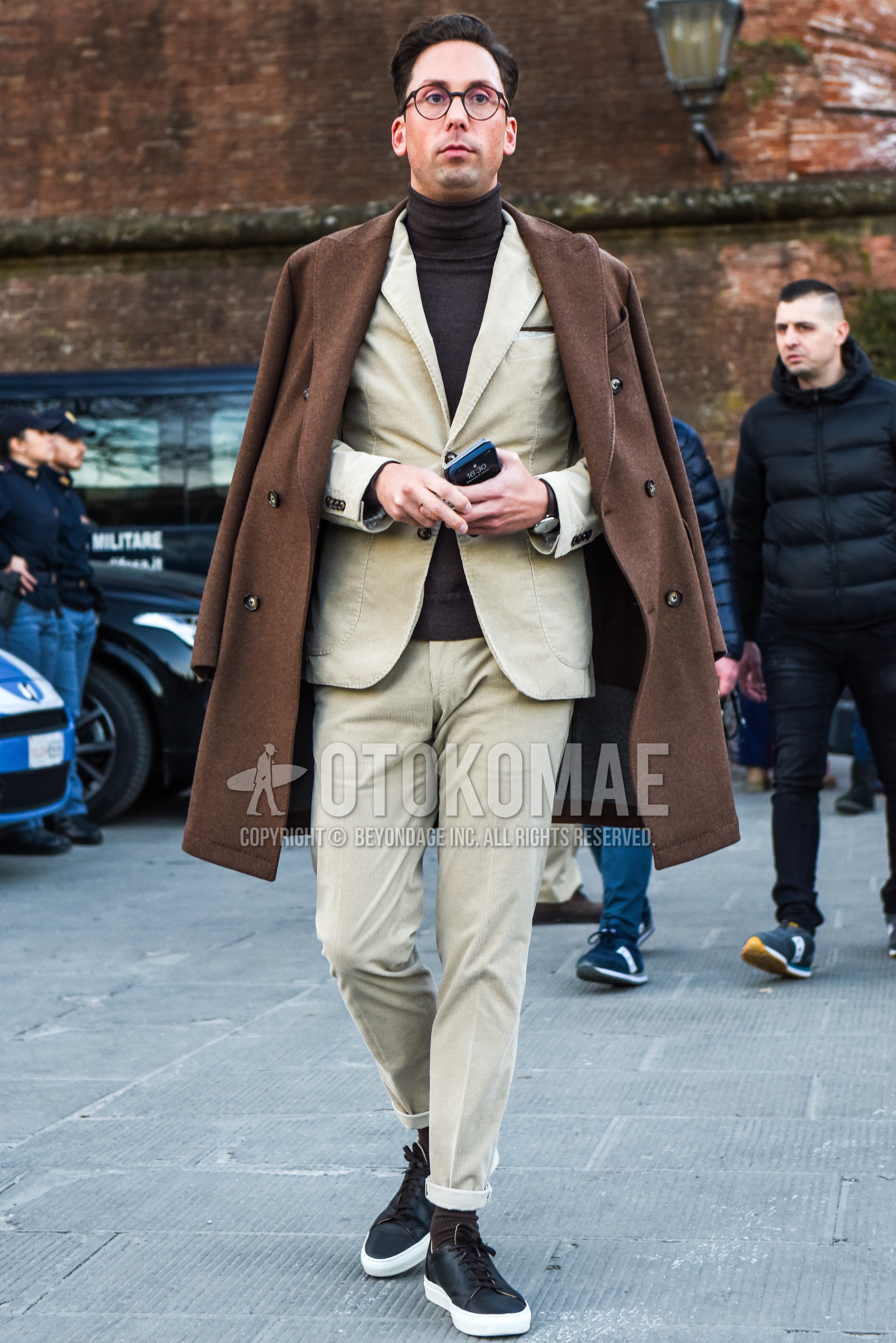 Men's autumn winter outfit with brown tortoiseshell glasses, beige plain chester coat, brown plain turtleneck knit, brown plain socks, black low-cut sneakers, beige plain suit.