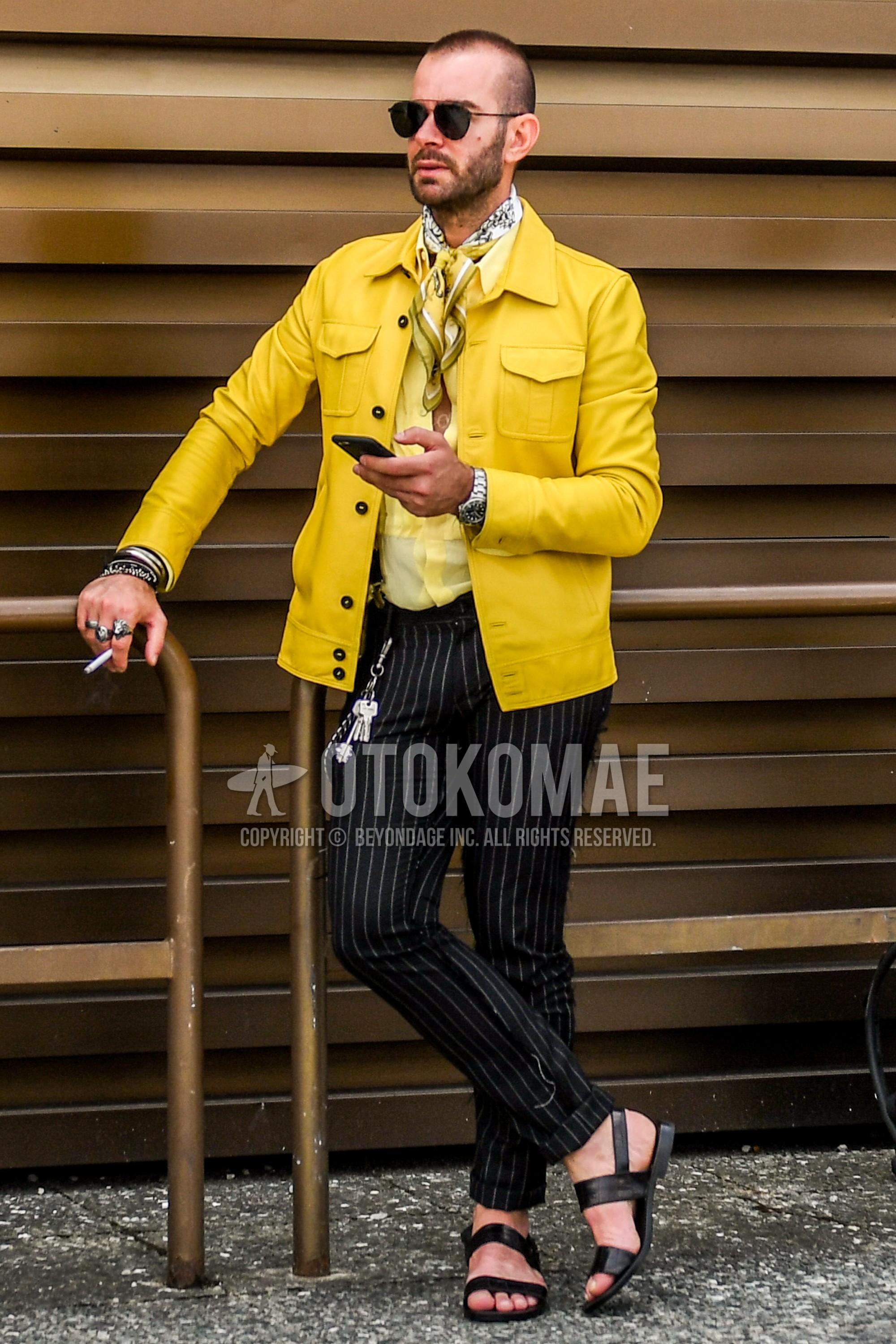 Men's spring summer autumn outfit with plain sunglasses, yellow white scarf scarf, yellow plain leather jacket, plain trucker jacket, yellow plain shirt, navy stripes ankle pants, black leather sandals.