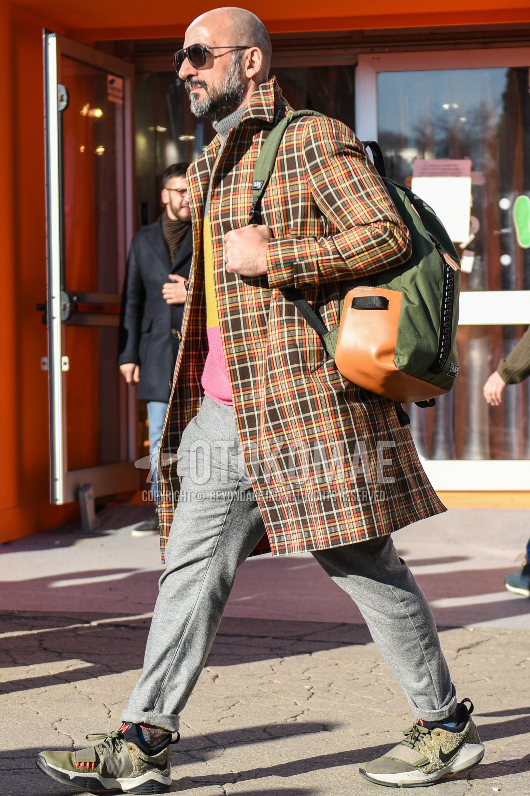 Men's autumn winter outfit with black plain sunglasses, multi-color check stenkarrer coat, multi-color tops/innerwear sweater, gray plain slacks, multi-color socks socks, olive green low-cut sneakers, olive green plain backpack.
