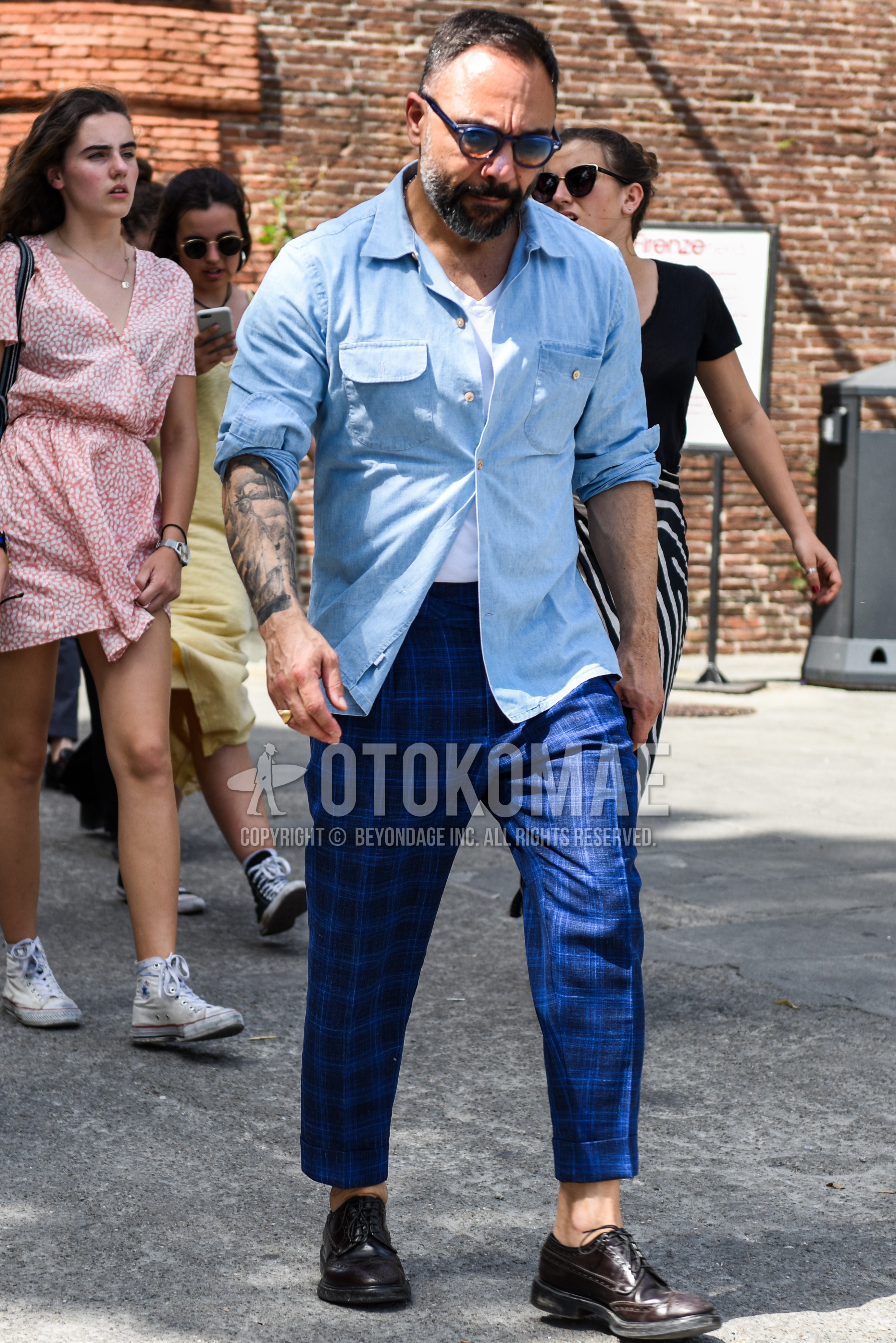 Men's spring summer outfit with navy plain sunglasses, light blue plain denim shirt/chambray shirt, white plain t-shirt, blue check slacks, blue check ankle pants, brown wing-tip shoes leather shoes.