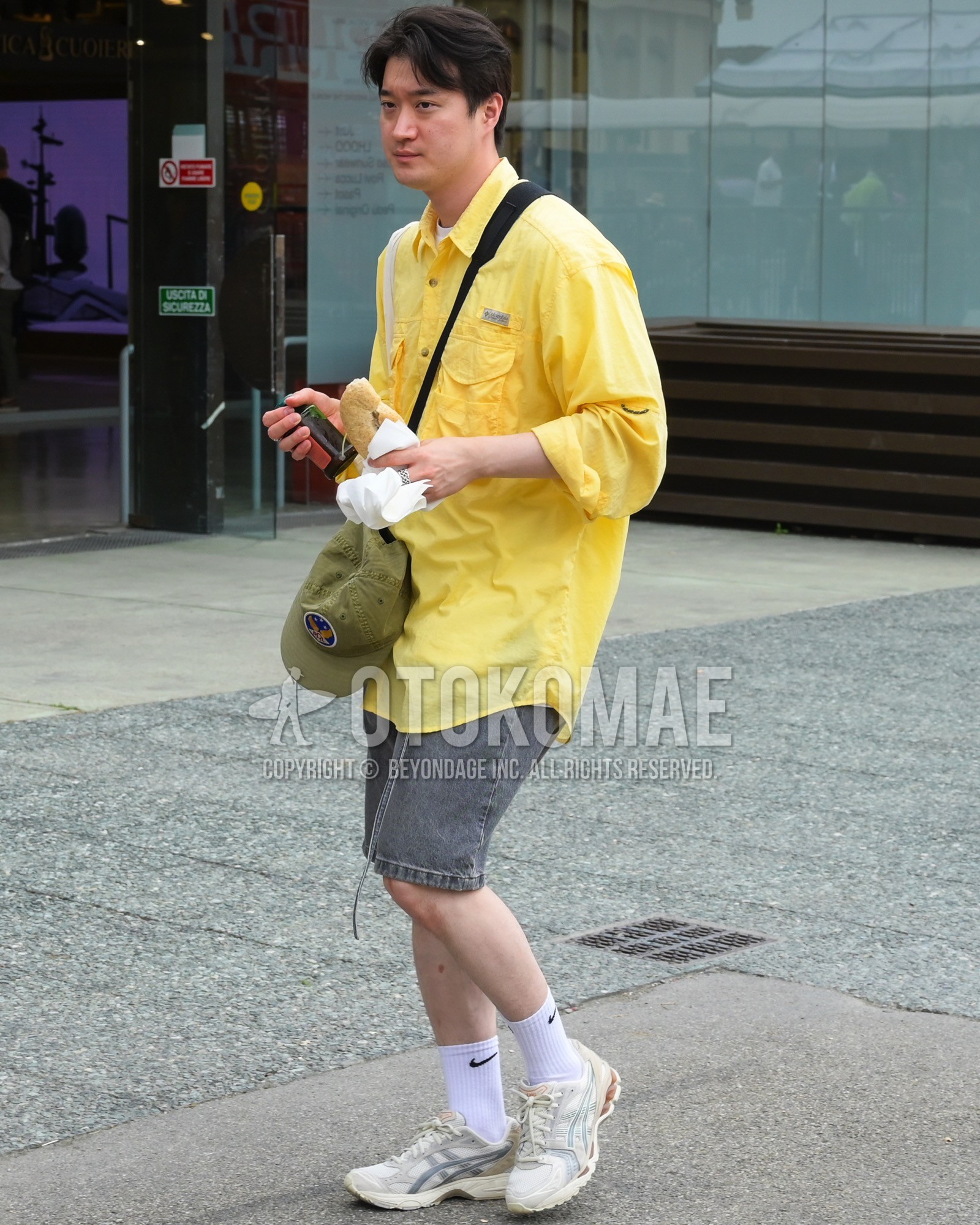 Men's spring summer outfit with yellow plain shirt, white plain t-shirt, gray plain short pants, white plain socks, white low-cut sneakers, black plain shoulder bag.
