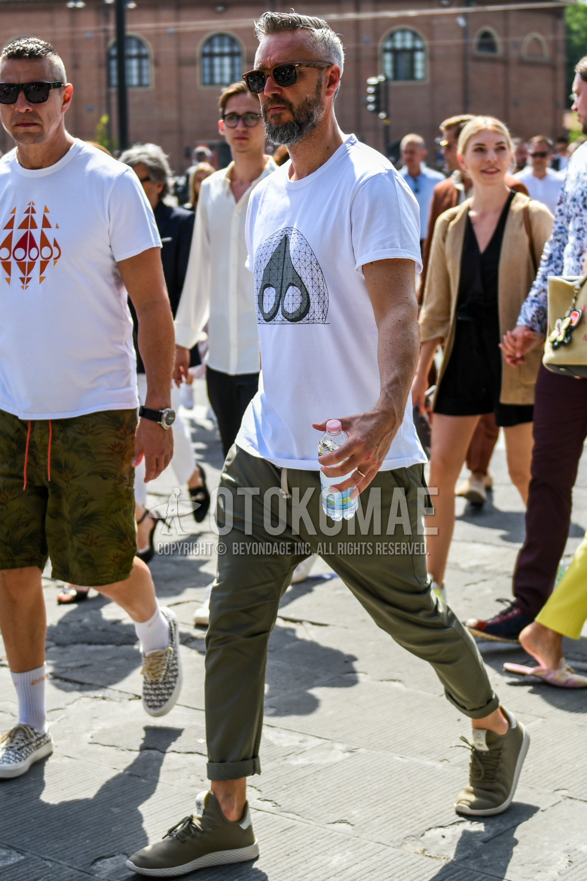 Men's summer outfit with brown plain sunglasses, white deca logo t-shirt, olive green plain easy pants, olive green low-cut sneakers.