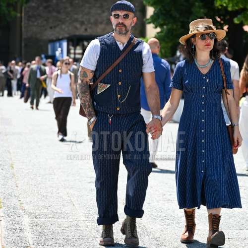 ネイビーキャップのベースボールキャップ、ゴールド無地のサングラス、ネイビートップス/インナーのカジュアルベスト、バンドカラーの白無地のシャツ、ネイビーボトムスのコットンパンツ、グレーワークのブーツ、レザーのブラウン無地のショルダーバッグ、ネイビースーツのカジュアルセットアップを合わせた夏春のメンズコーデ・着こなし。