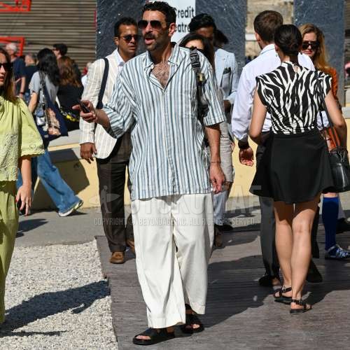 ティアドロップのクリア無地のサングラス、白・ブルーストライプのシャツ、白無地のチノパン、白無地のワイドパンツ、黒レザーサンダル、黒シャワーサンダル、黒無地のバックパックを合わせた夏春のメンズコーデ・着こなし。