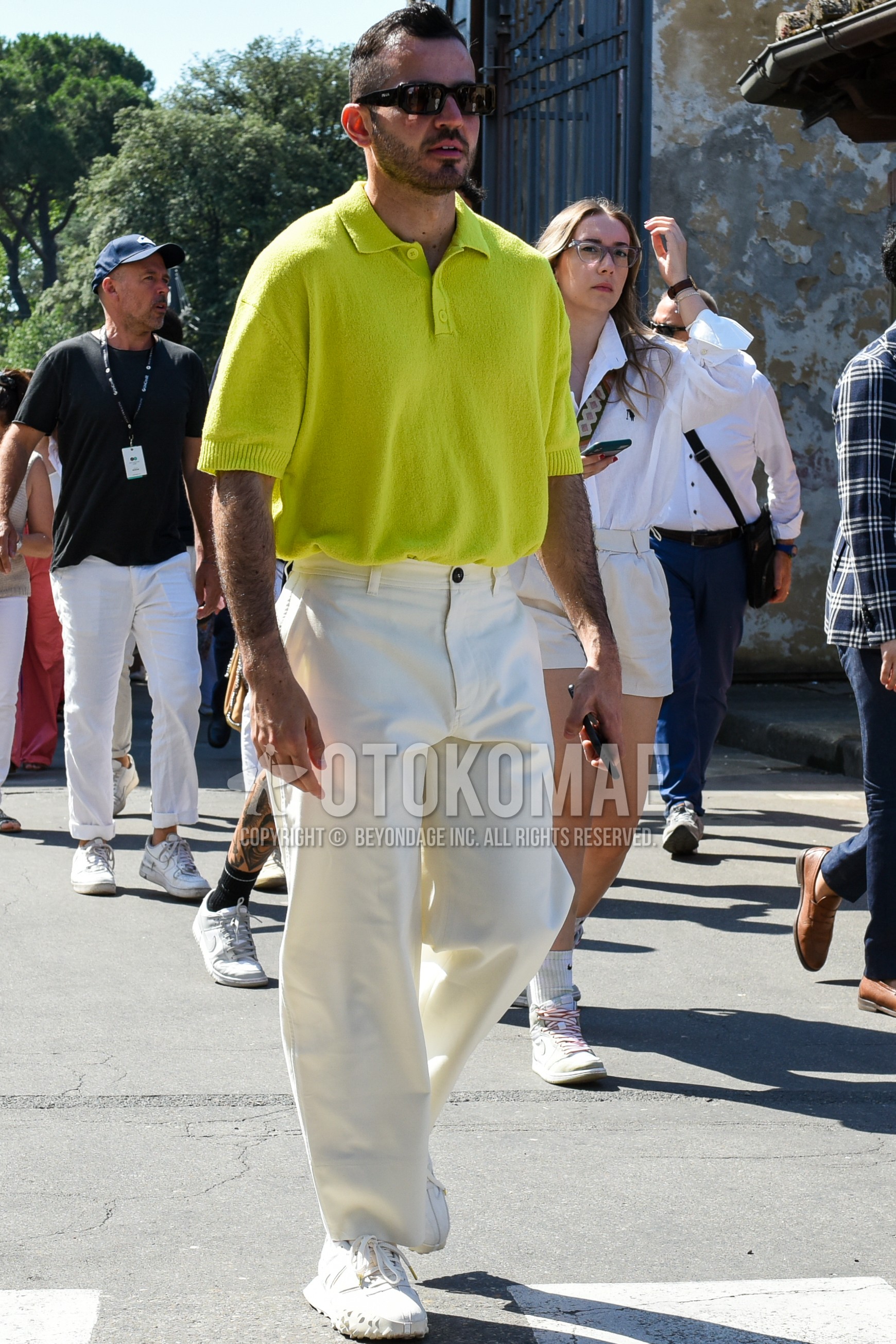 Men's spring summer outfit with black plain sunglasses, yellow green plain polo shirt, white plain wide pants, white low-cut sneakers.