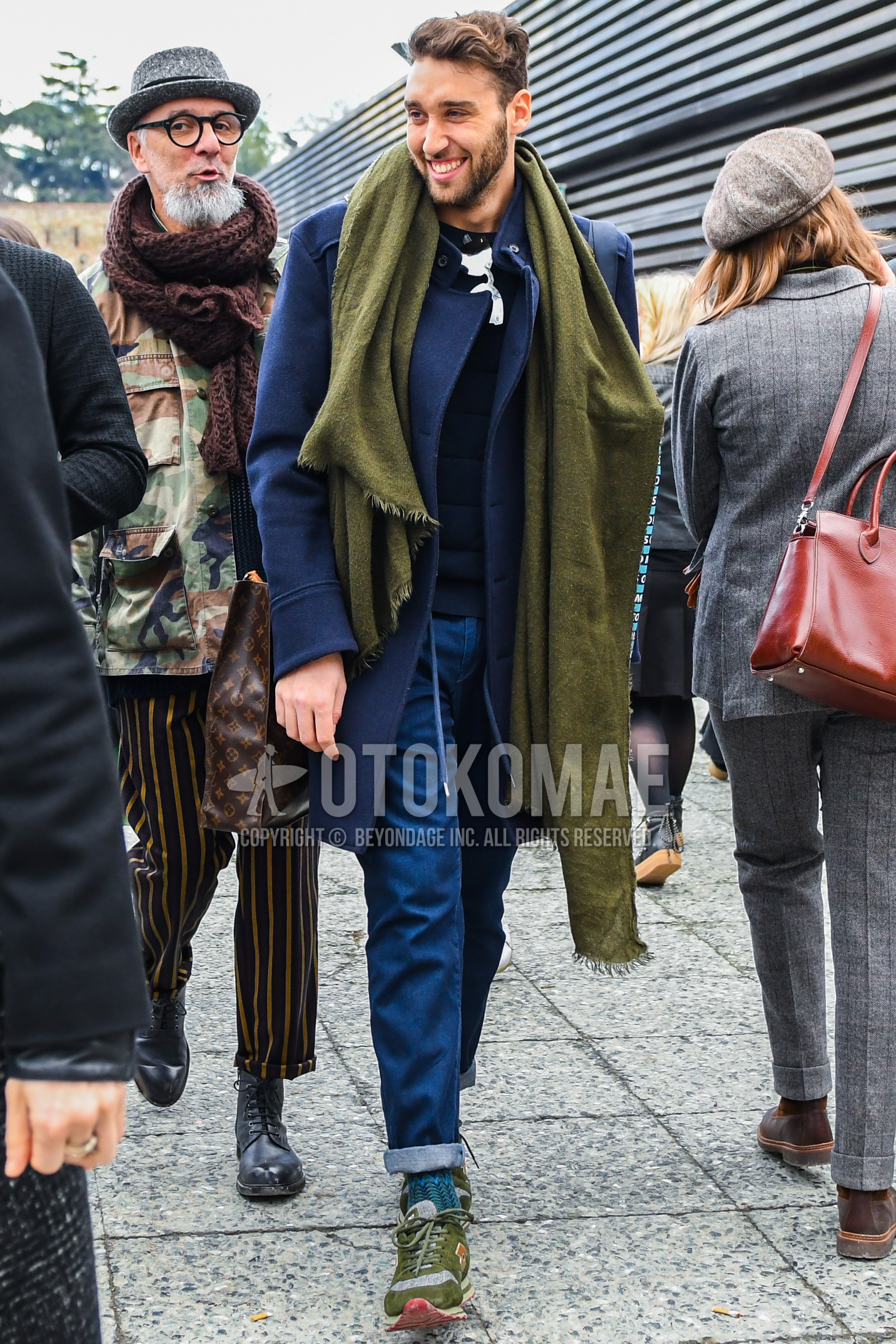 Men's autumn winter outfit with olive green plain scarf, navy plain chester coat, blue plain denim/jeans, blue socks socks, olive green low-cut sneakers.