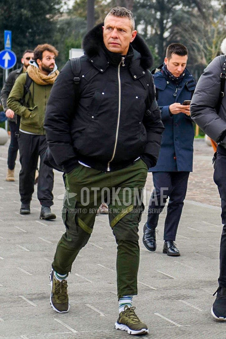 Men's winter outfit with black plain hooded coat, olive green plain cargo pants, white horizontal stripes socks, olive green low-cut sneakers.