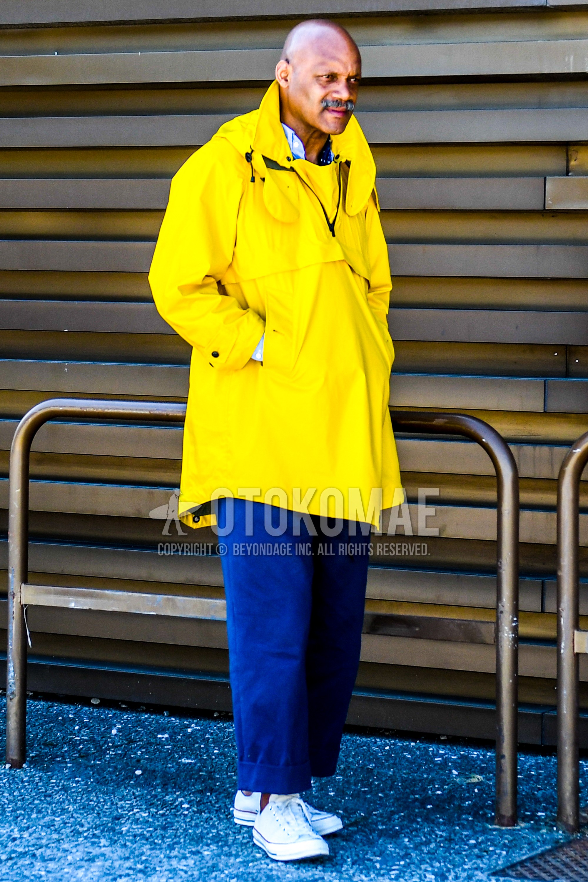 Men's spring autumn outfit with yellow plain hooded coat, blue plain wide pants, white low-cut sneakers.