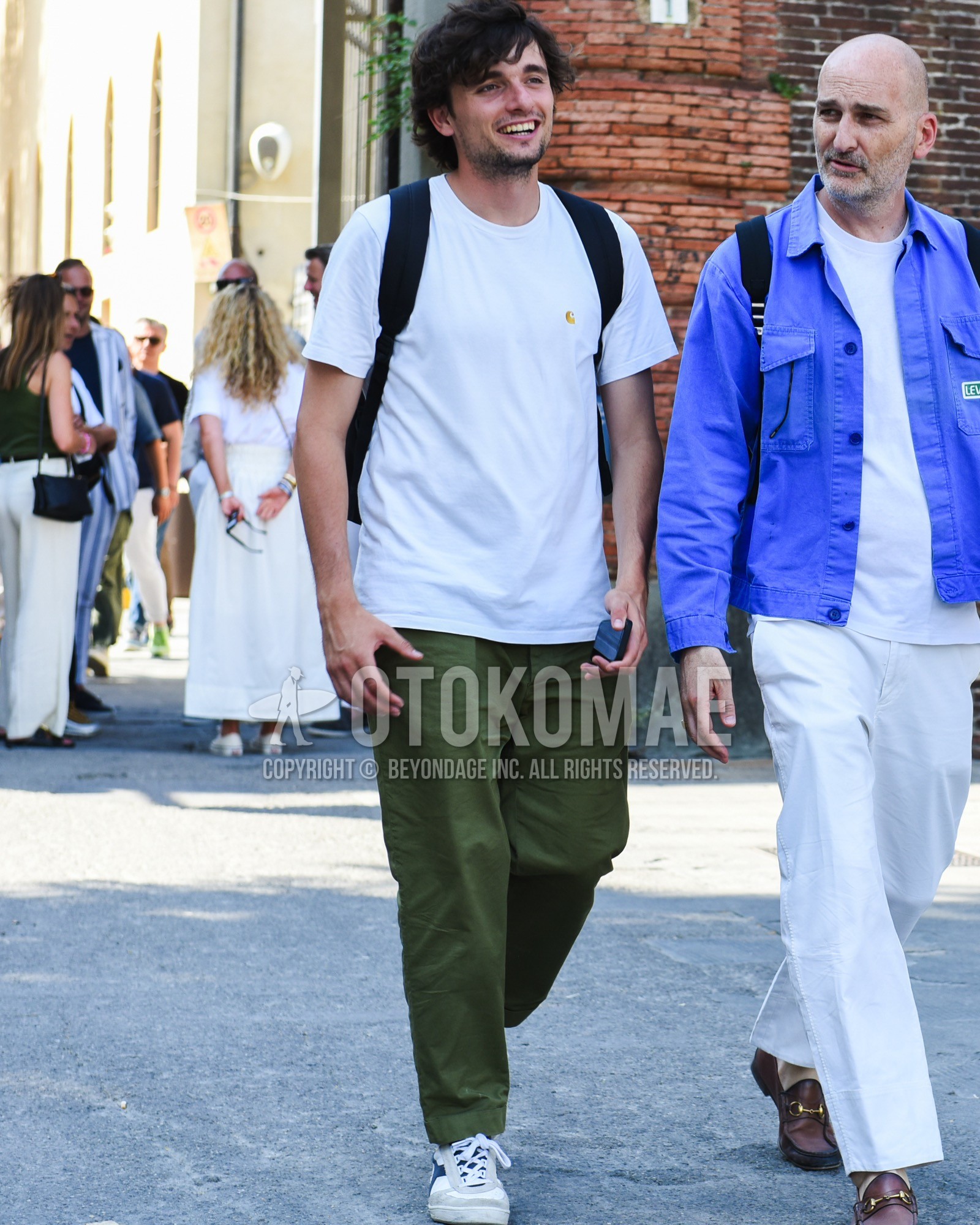 Men's spring summer outfit with white one point t-shirt, olive green plain chinos, white gray low-cut sneakers, navy plain backpack.