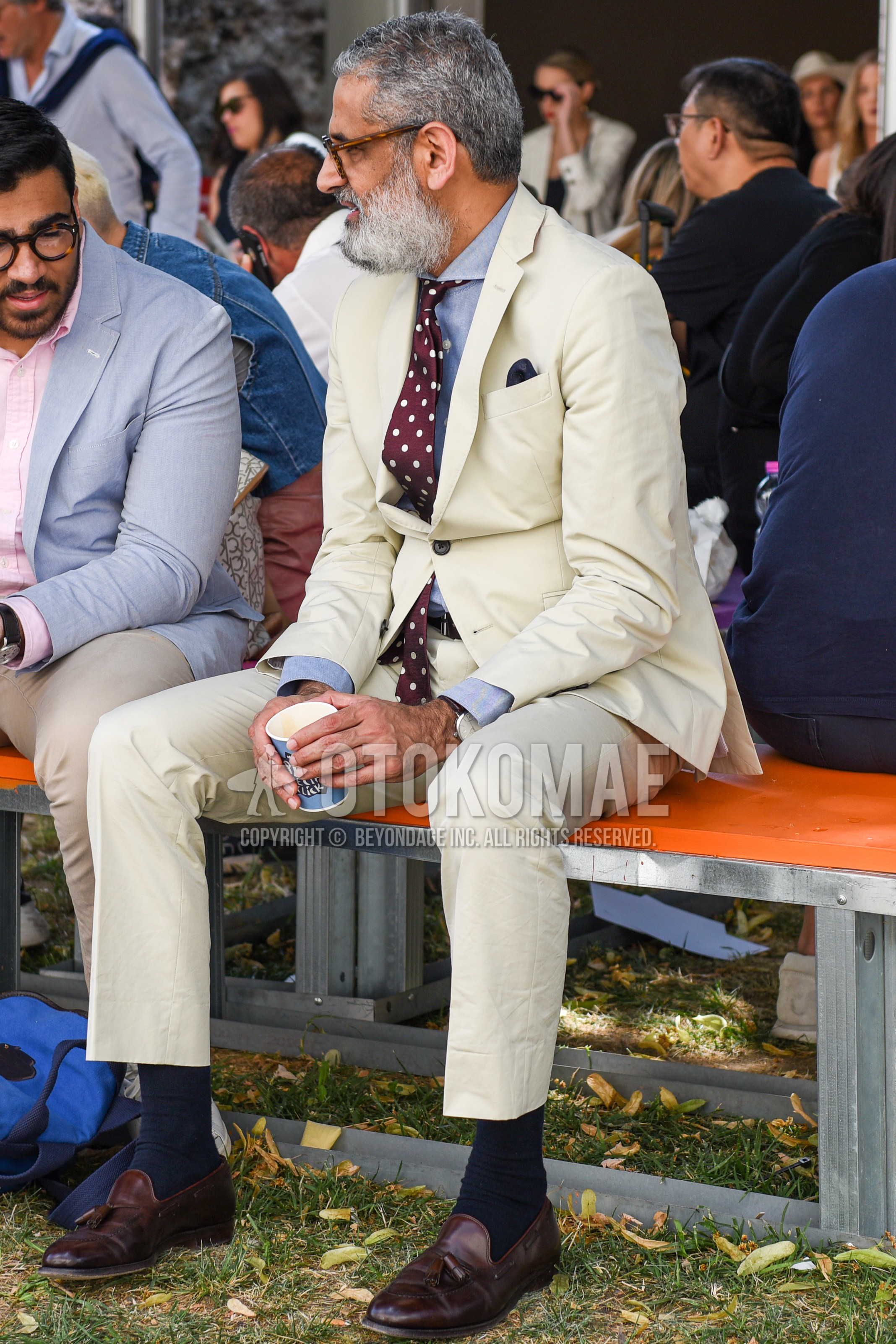 Men's spring autumn outfit with brown tortoiseshell glasses, gray plain shirt, black plain socks, brown tassel loafers leather shoes, white plain suit, red dots necktie.
