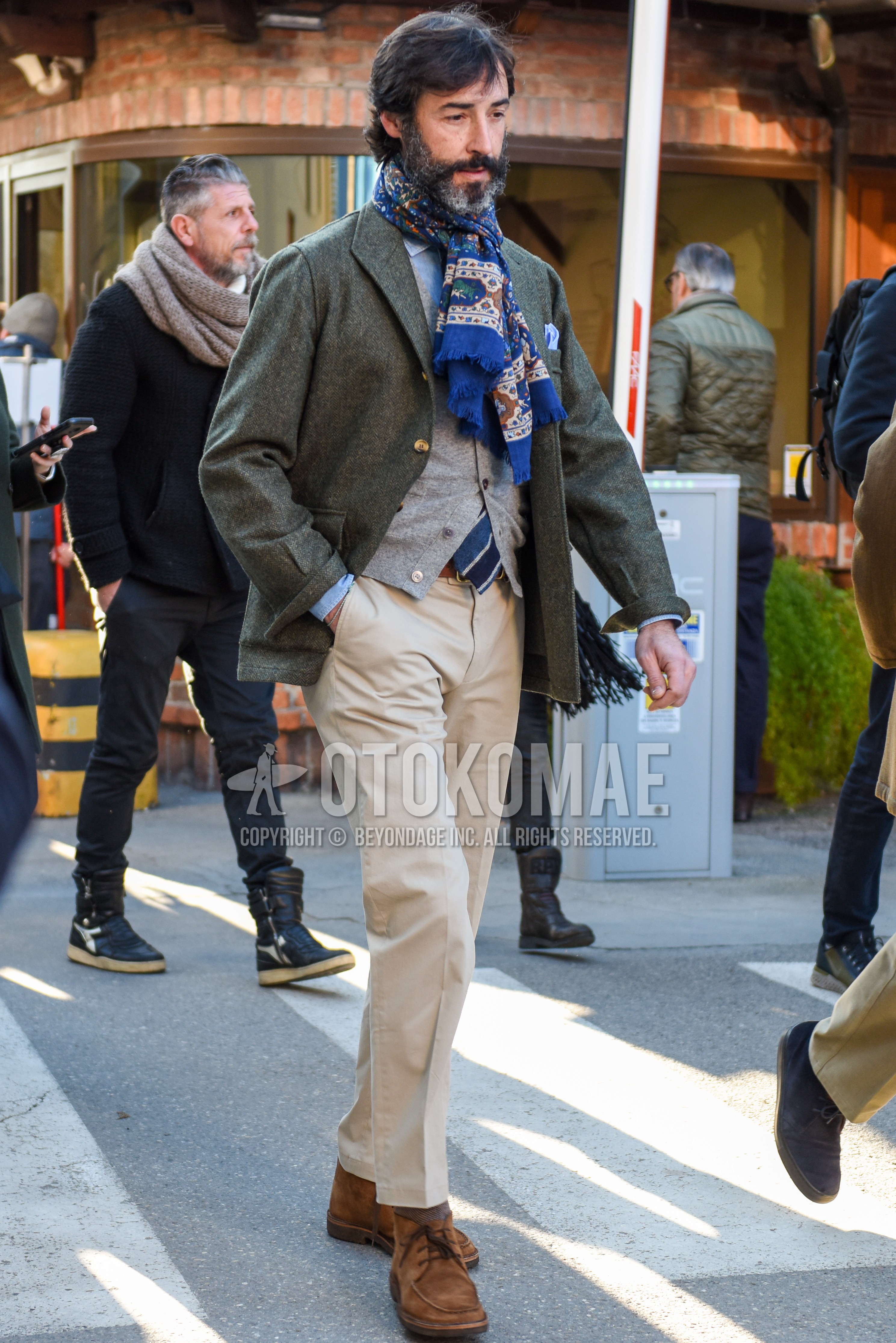 Men's autumn winter outfit with gray scarf scarf, gray plain shirt jacket, gray plain cardigan, light blue plain shirt, beige plain chinos, beige plain cropped pants, beige plain socks, brown chukka boots.