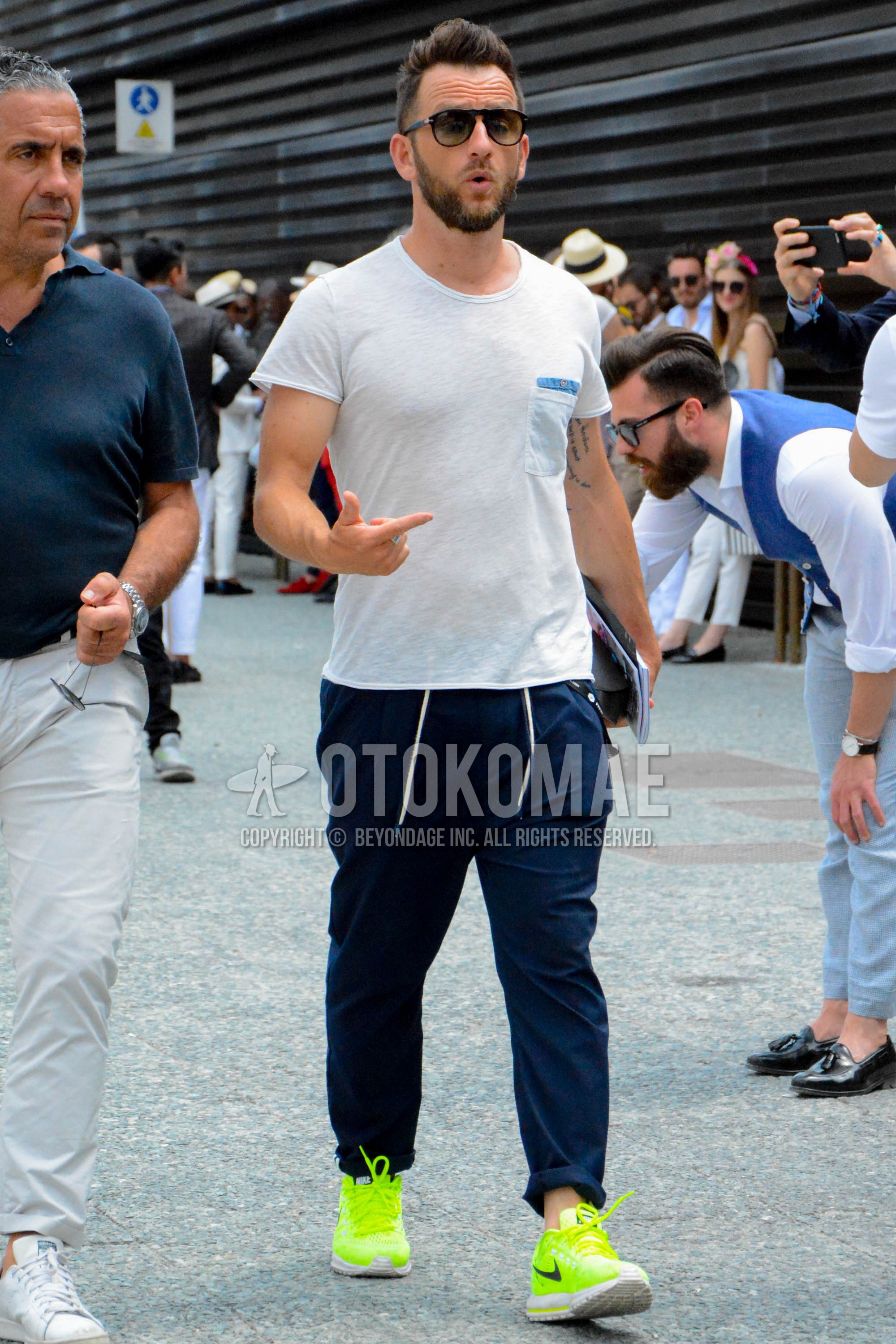 Men's spring summer outfit with black plain sunglasses, white plain t-shirt, navy plain chinos, navy plain easy pants, yellow low-cut sneakers.