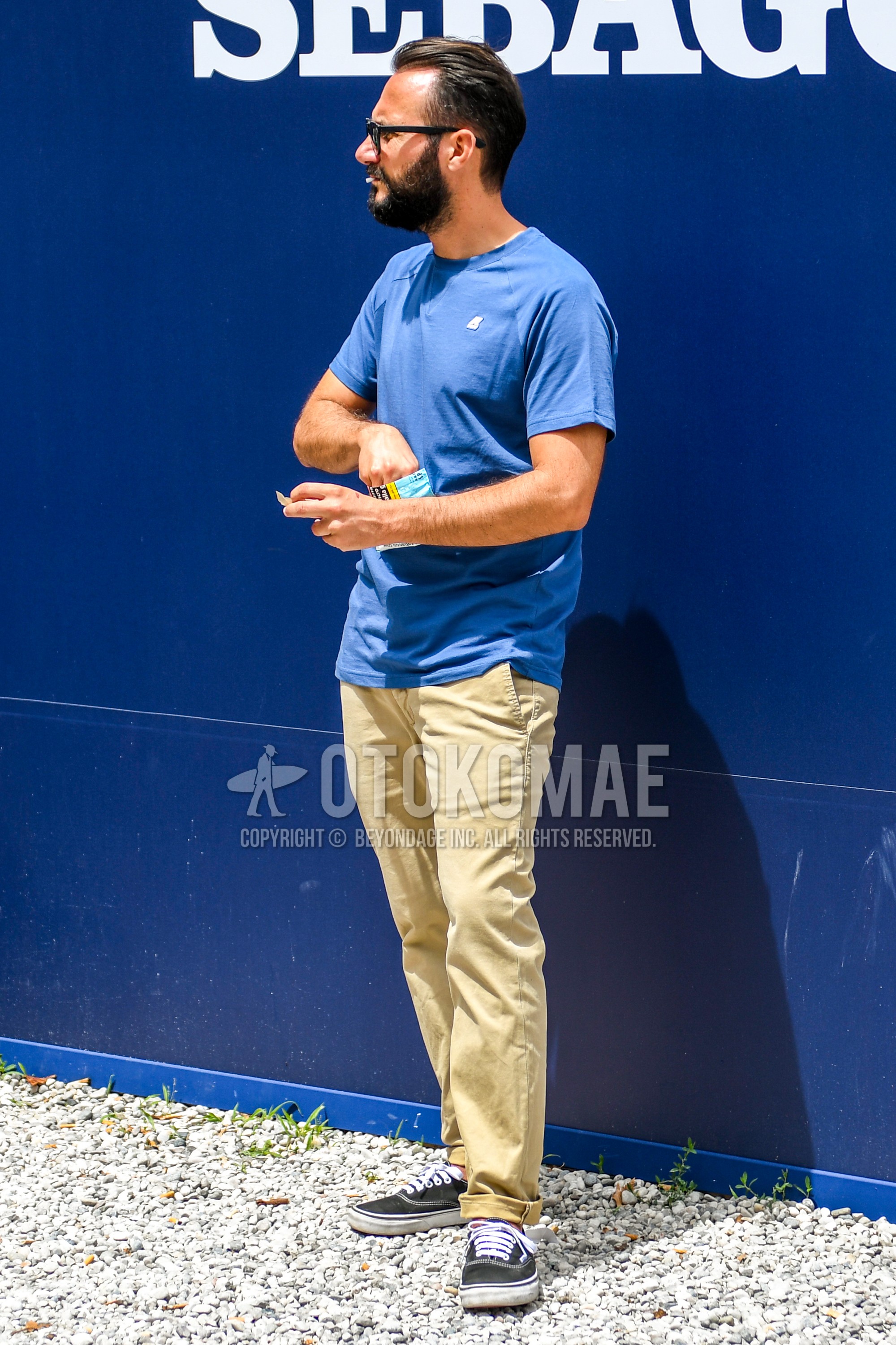 Men's summer outfit with plain sunglasses, blue one point t-shirt, beige plain chinos, black low-cut sneakers.