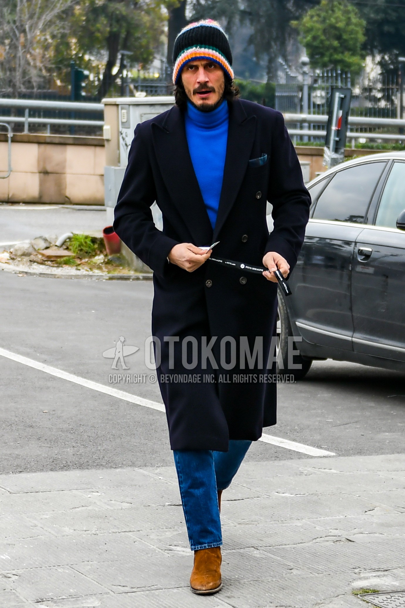 Men's autumn winter outfit with multi-color plain knit cap, black plain chester coat, blue plain turtleneck knit, blue plain denim/jeans, beige side-gore boots.